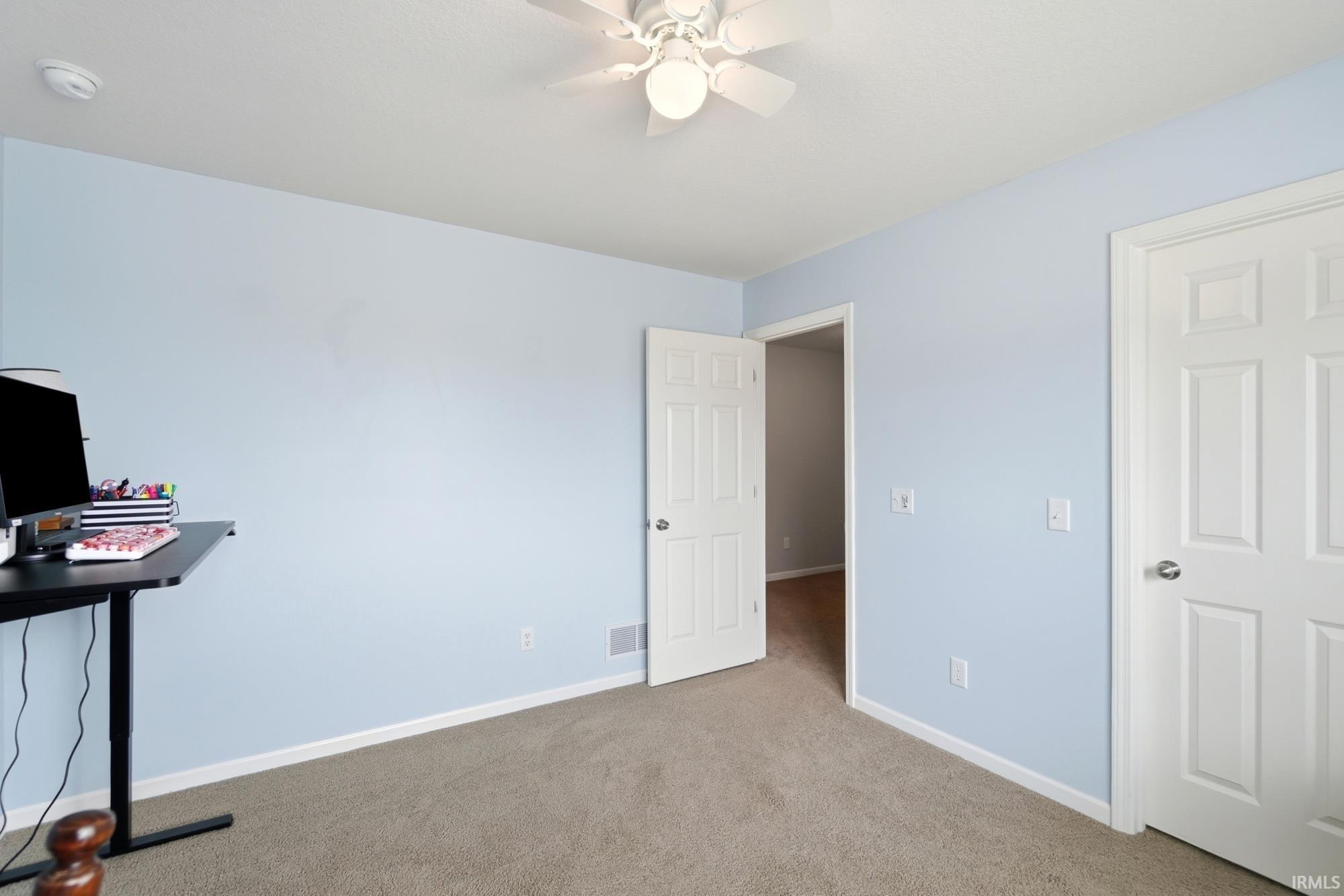 Carpeted room featuring light blue walls, white trim, and a white ceiling fan with integrated lighting