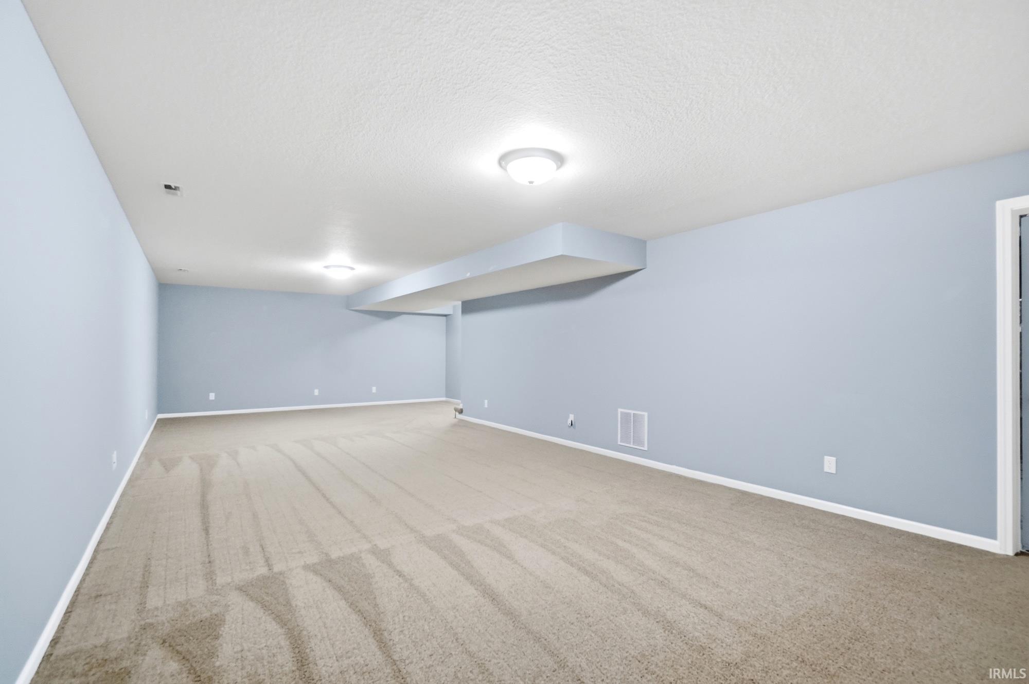 Spacious room with light blue walls, neutral carpeting, and recessed ceiling lights