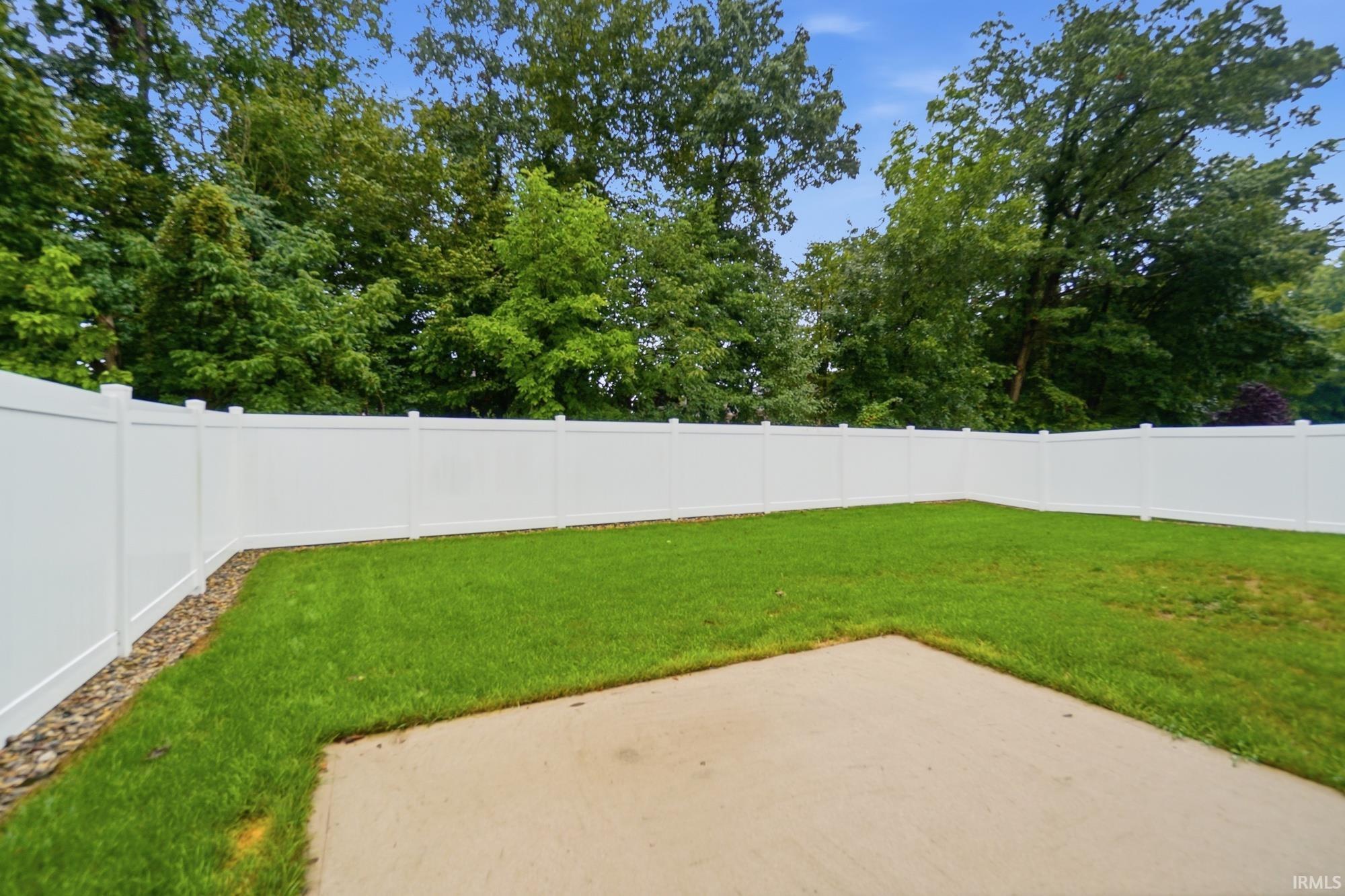 Expansive yard featuring a concrete patio, manicured lawn, and a white privacy fence