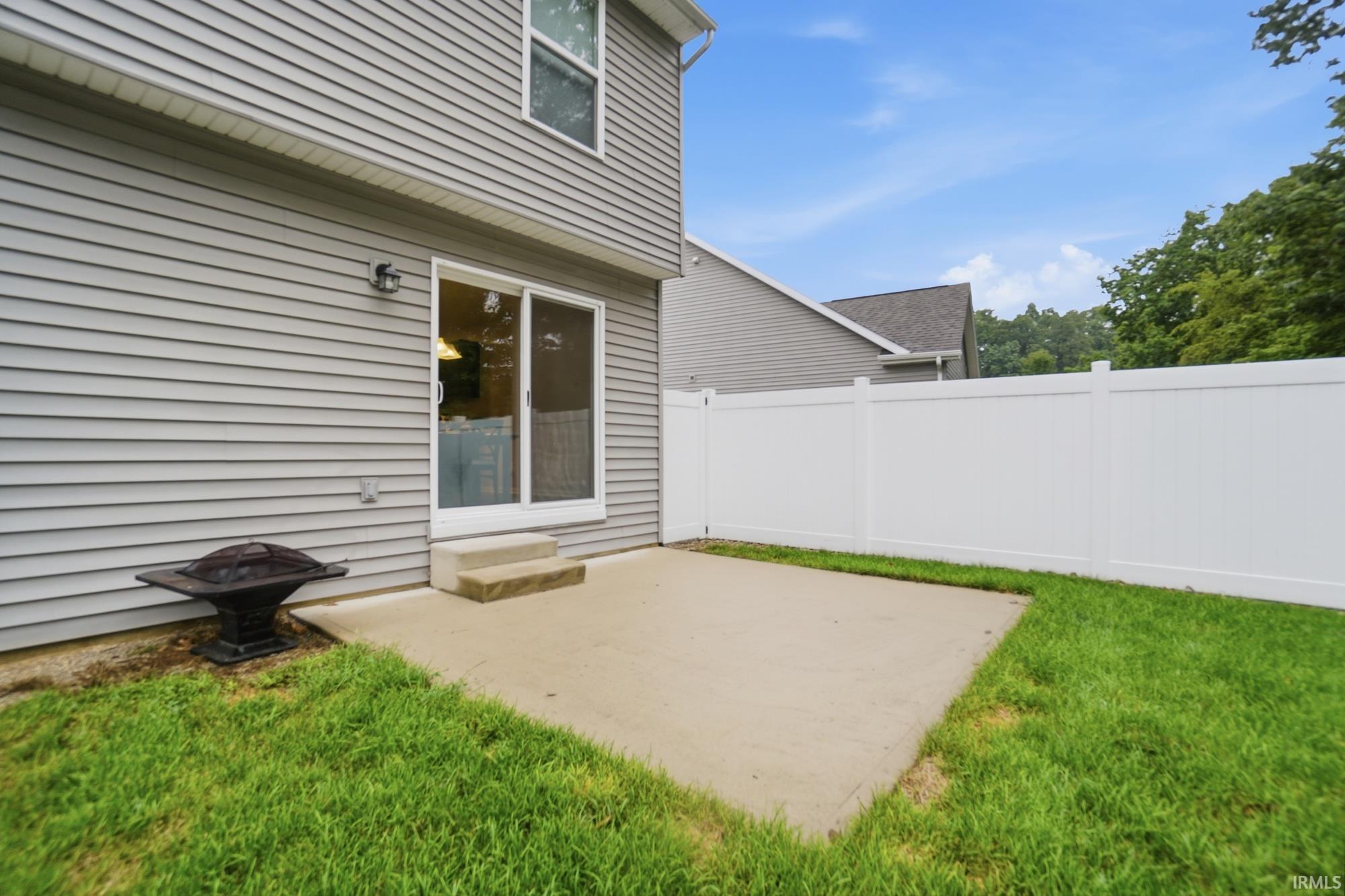 Concrete patio accessed by sliding glass doors, surrounded by a white privacy fence