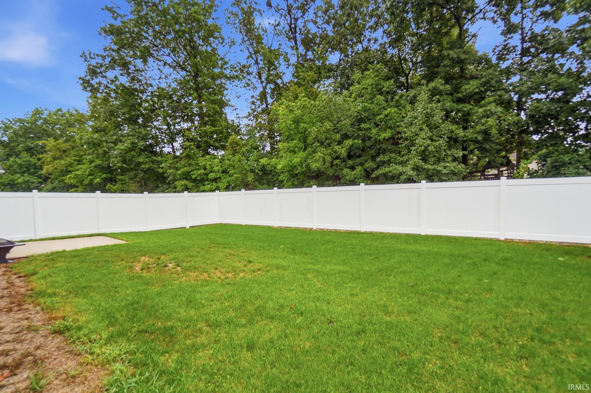 Expansive backyard with a manicured lawn, white privacy fencing, and a concrete patio area
