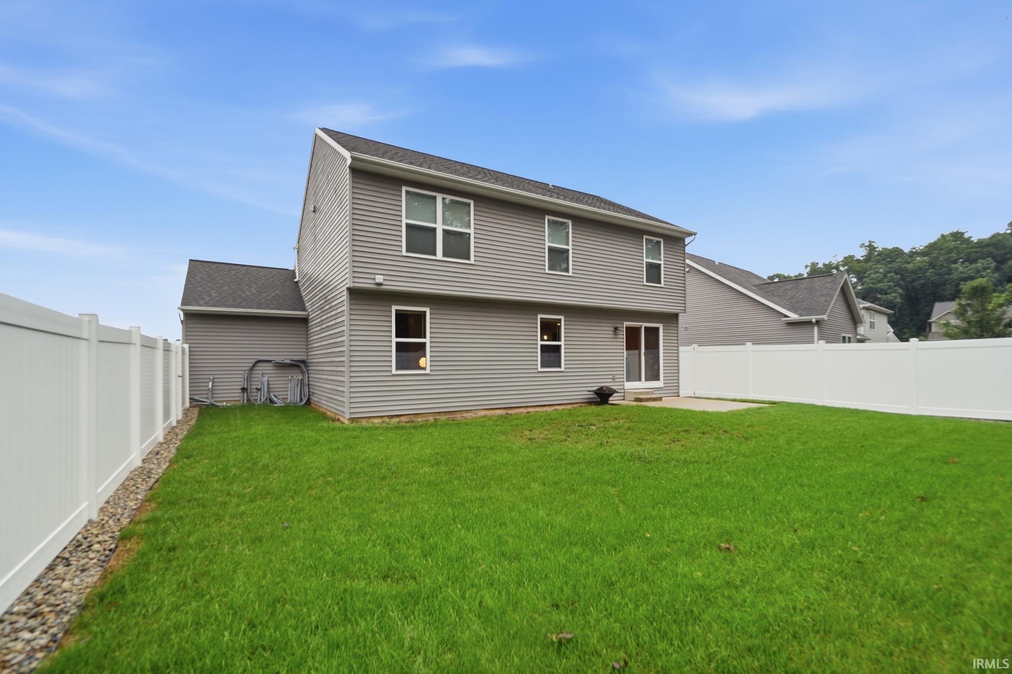 Expansive green lawn, white privacy fencing, concrete patio, sliding glass door, and gray horizontal siding