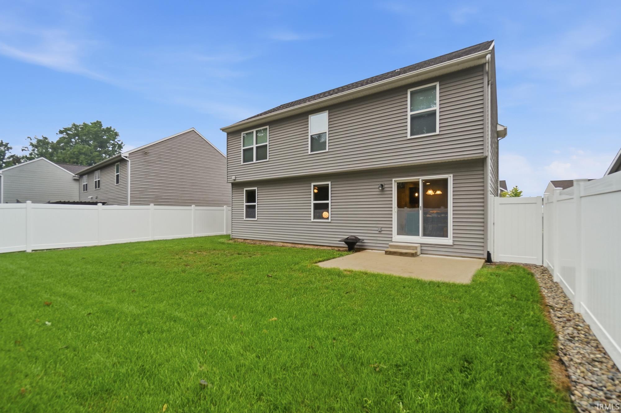 Expansive grassy yard with full privacy fencing, a concrete patio, and a sliding glass door entry