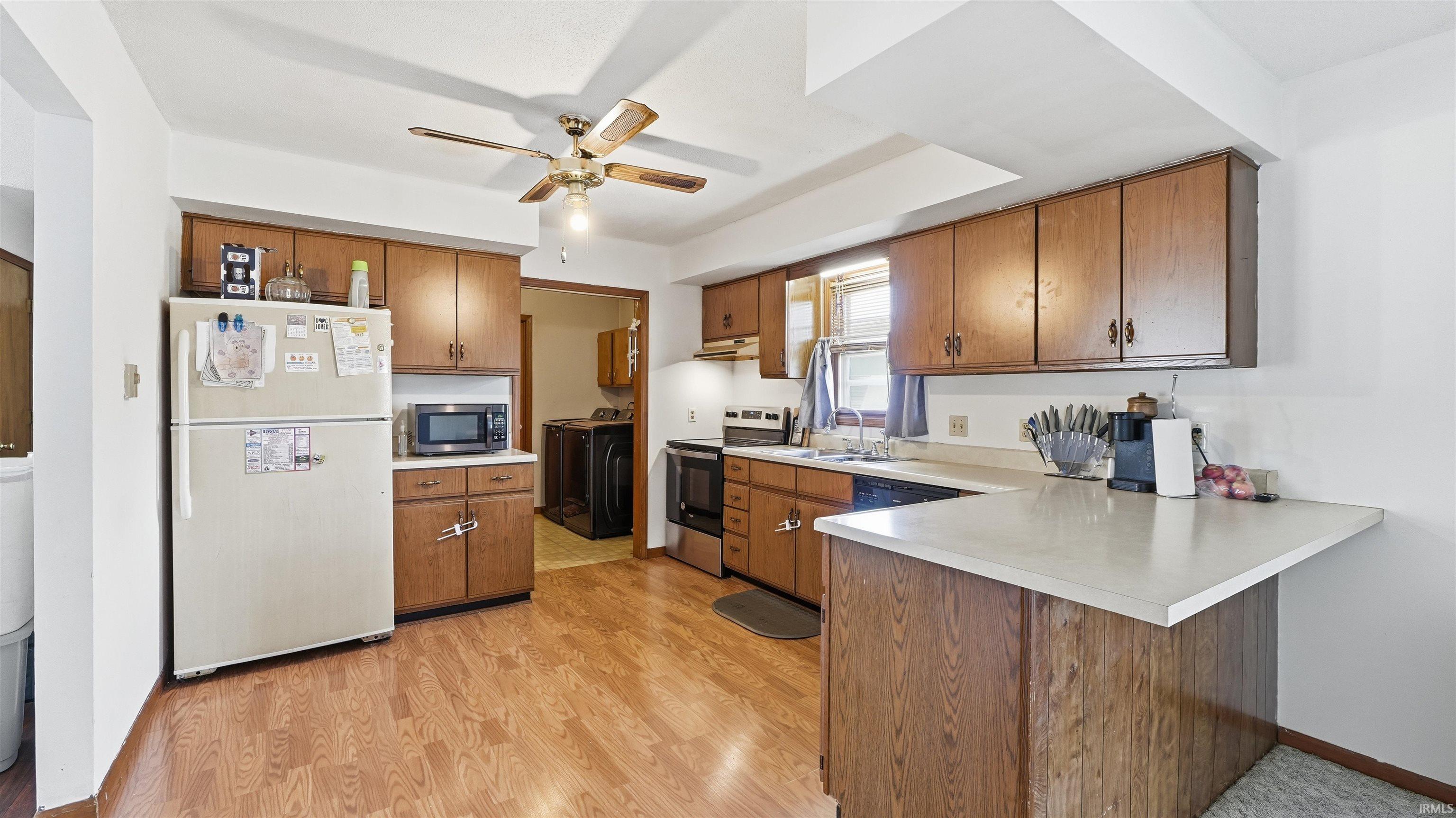 Kitchen featuring wood-finish flooring, ample cabinetry, a ceiling fan, and a pass-through counter