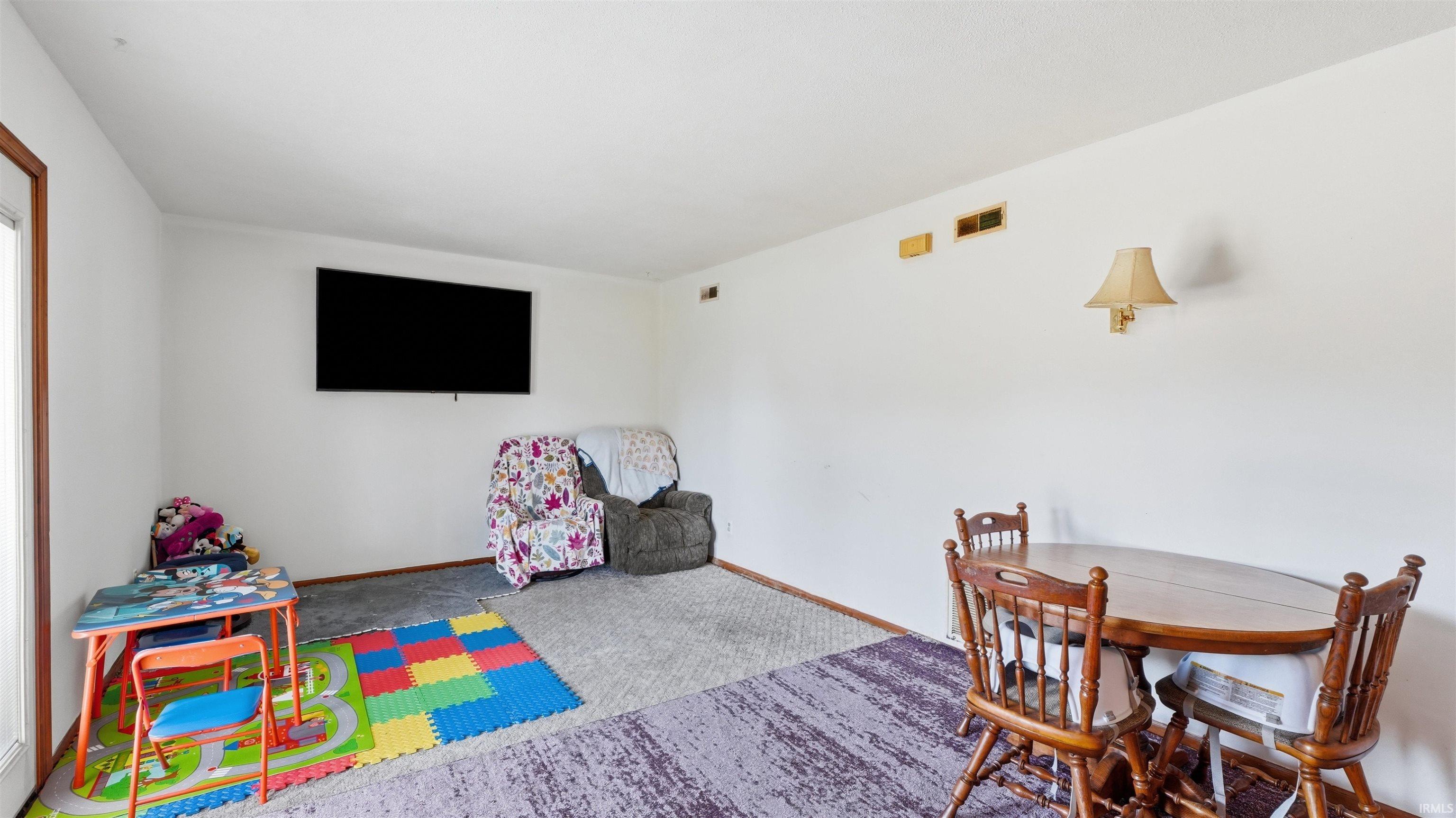 Living area featuring white walls, textured ceiling, a mounted wall light fixture, and floor vents