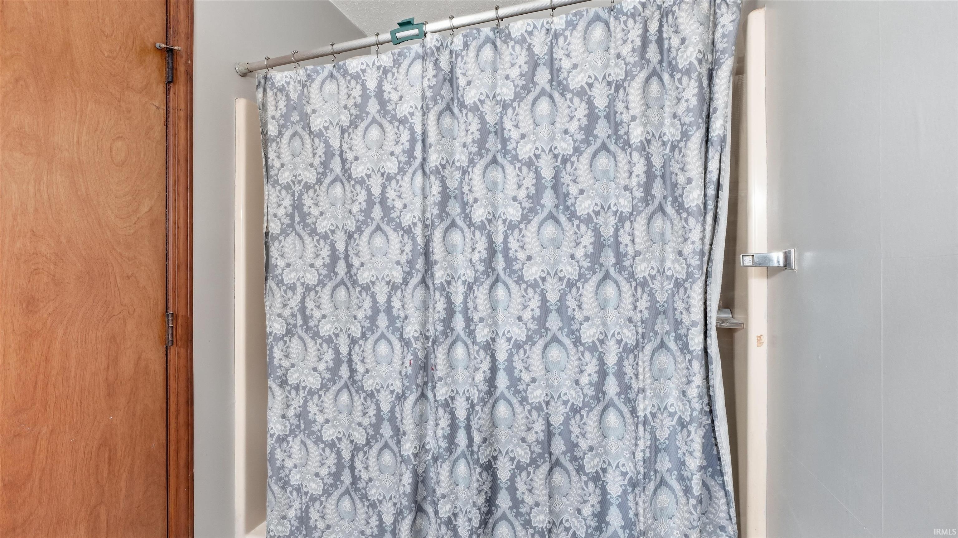 Shower with a patterned curtain, adjacent to a wooden door with visible hinges and latch