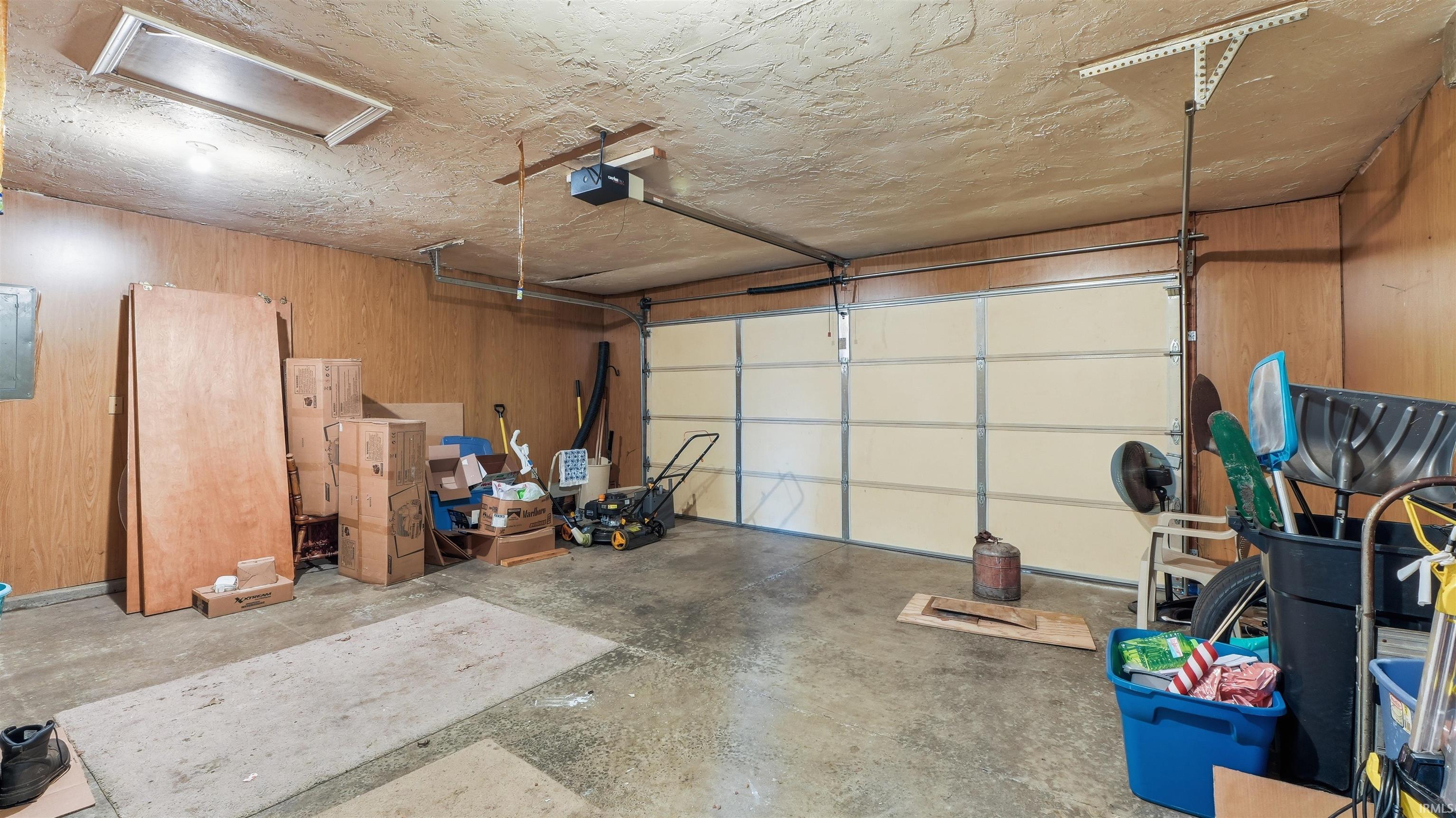 Single-bay garage featuring an overhead door, concrete flooring, wood-panel walls, and an overhead light fixture