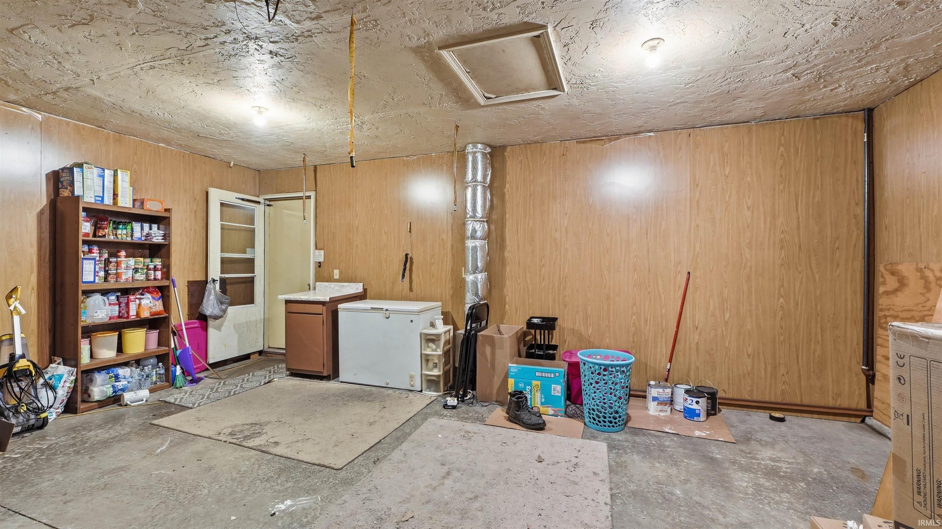 Utility room featuring wood-panel walls, concrete flooring, and an exposed ventilation system