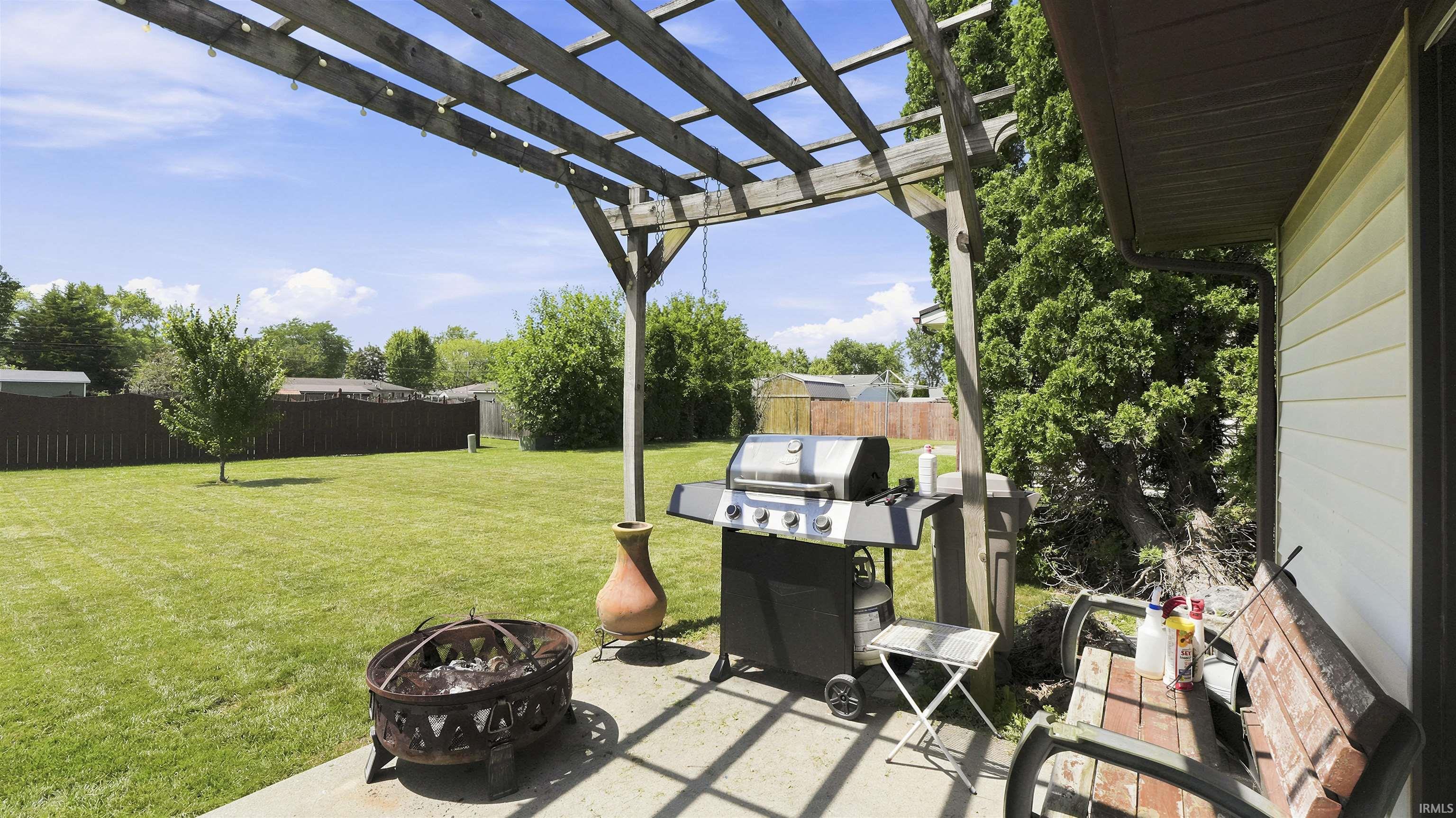 Expansive concrete patio with a wooden pergola, featuring a built-in fire pit