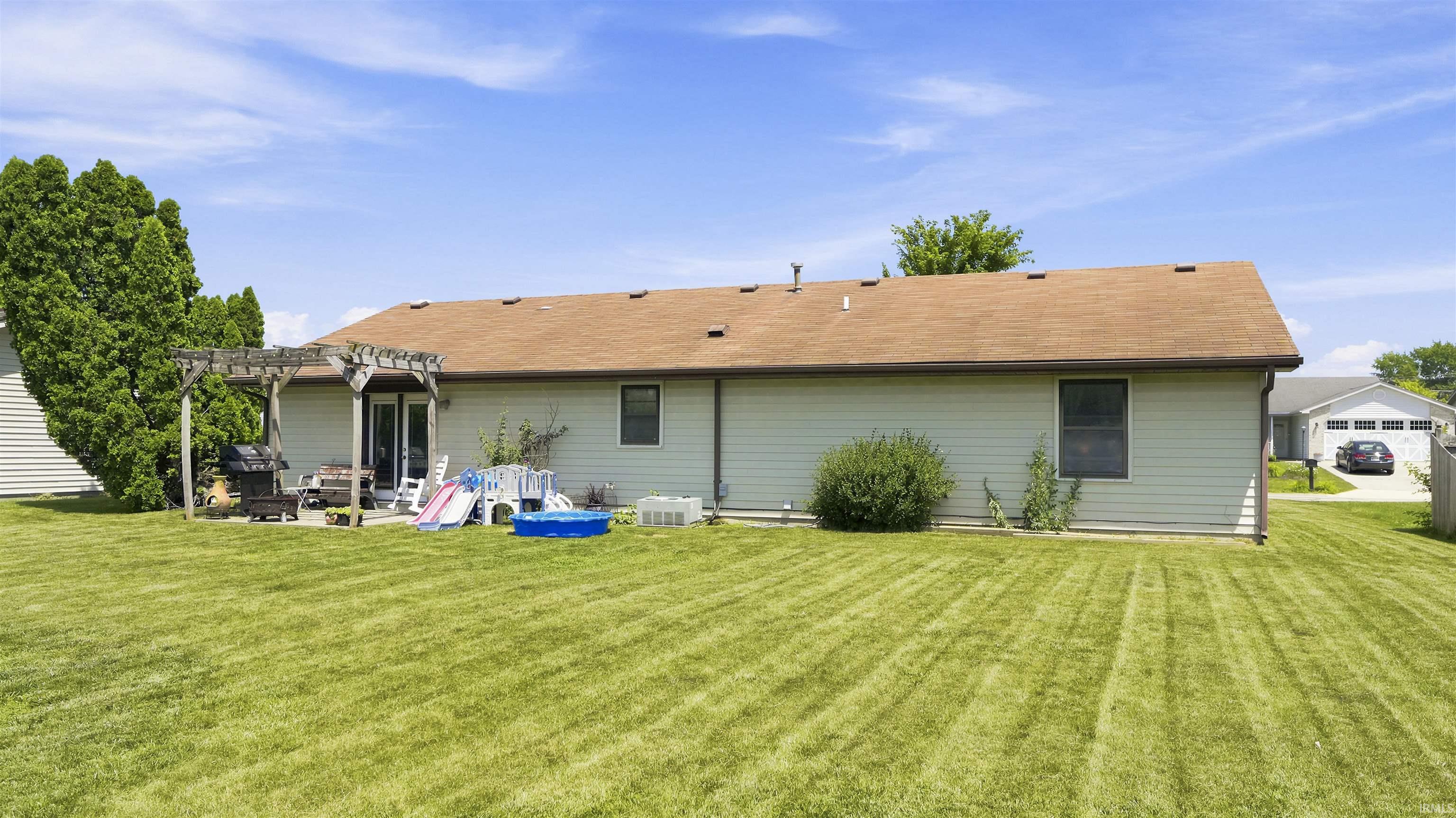 Expansive green lawn with a pergola-covered patio, French doors, and light-colored siding