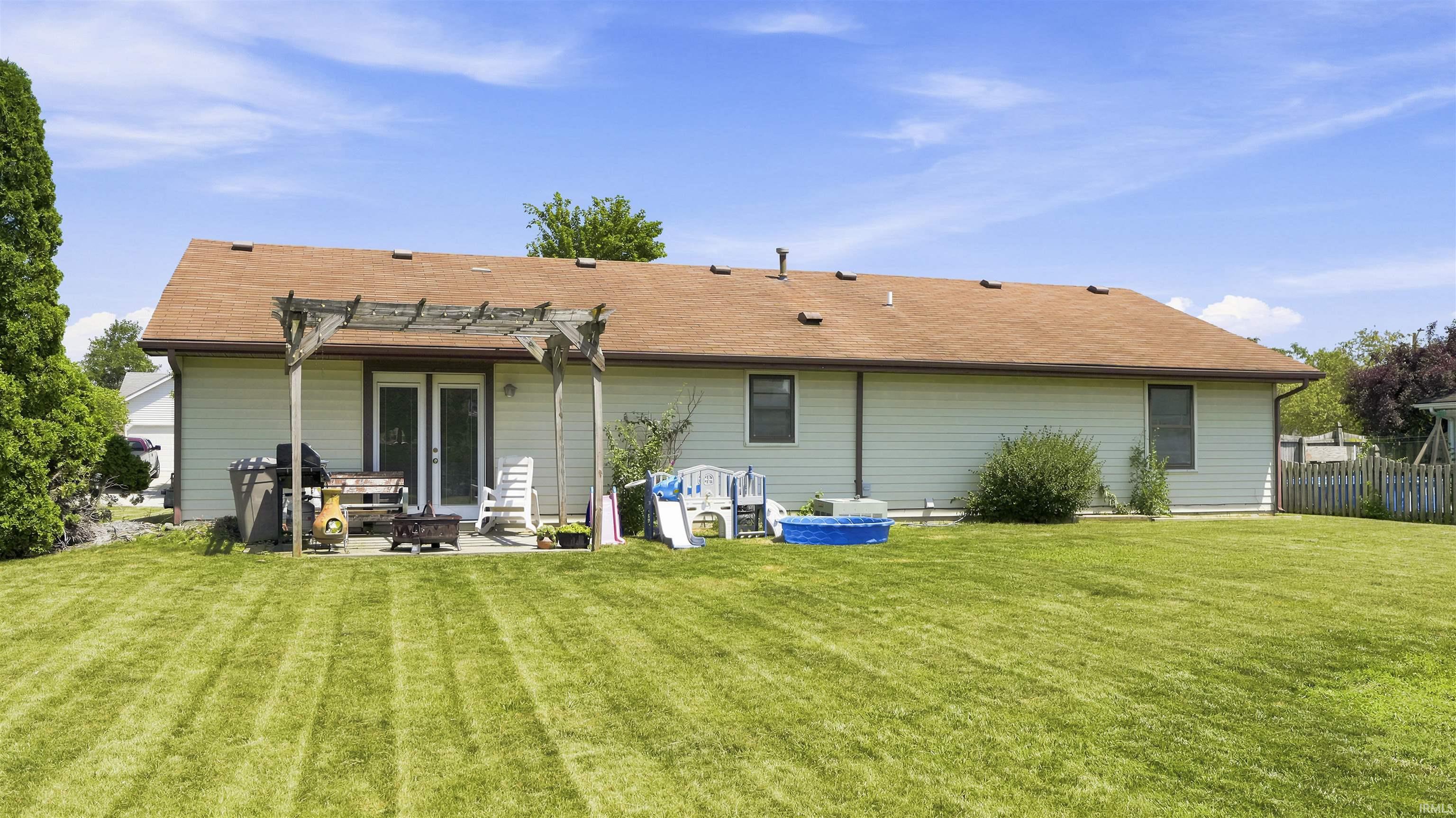 Expansive rear yard featuring a large patio with a wooden pergola, double French doors, and vinyl siding
