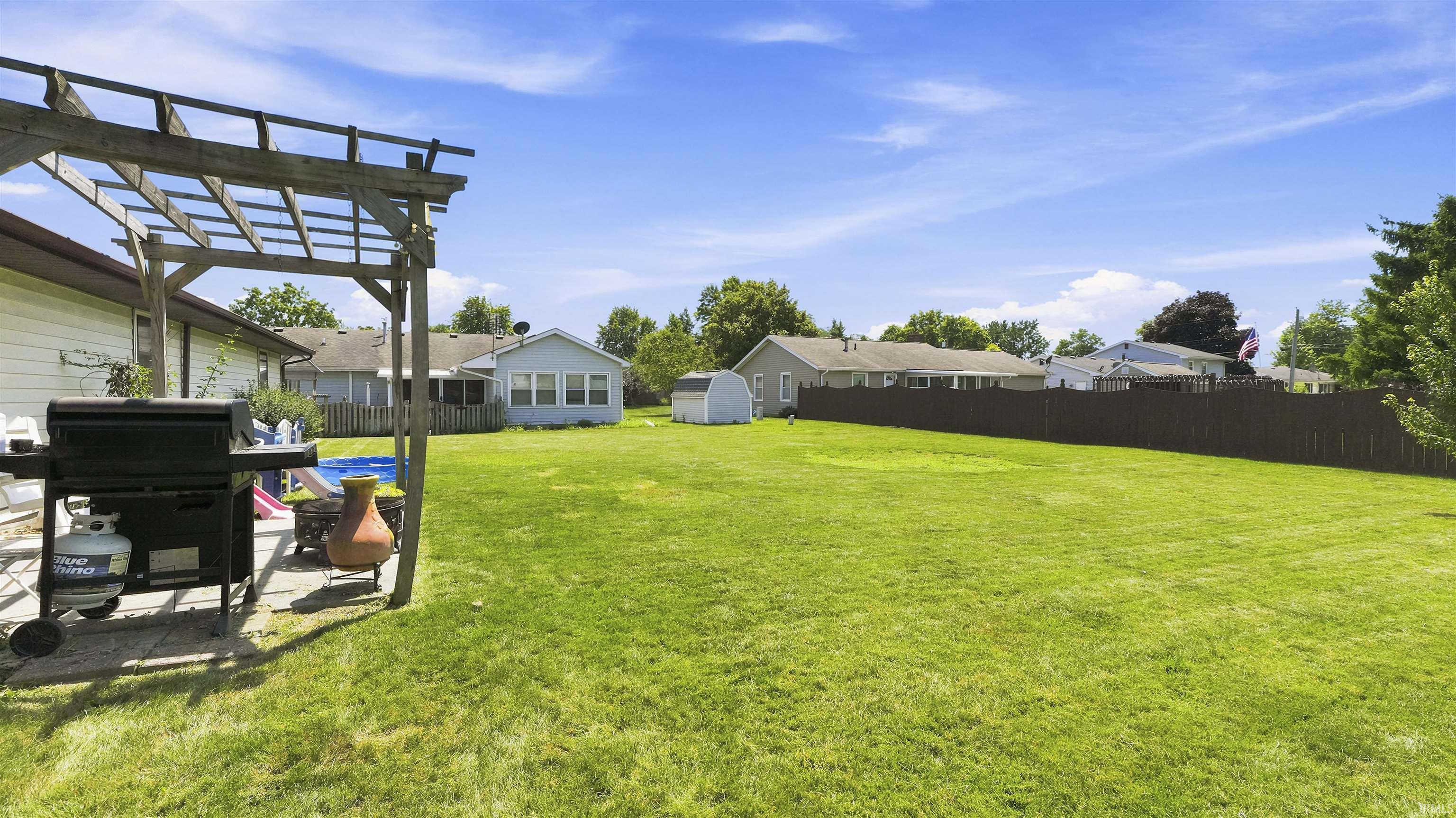 Expansive grass yard with a wood pergola, paver patio, and dark wood privacy fencing