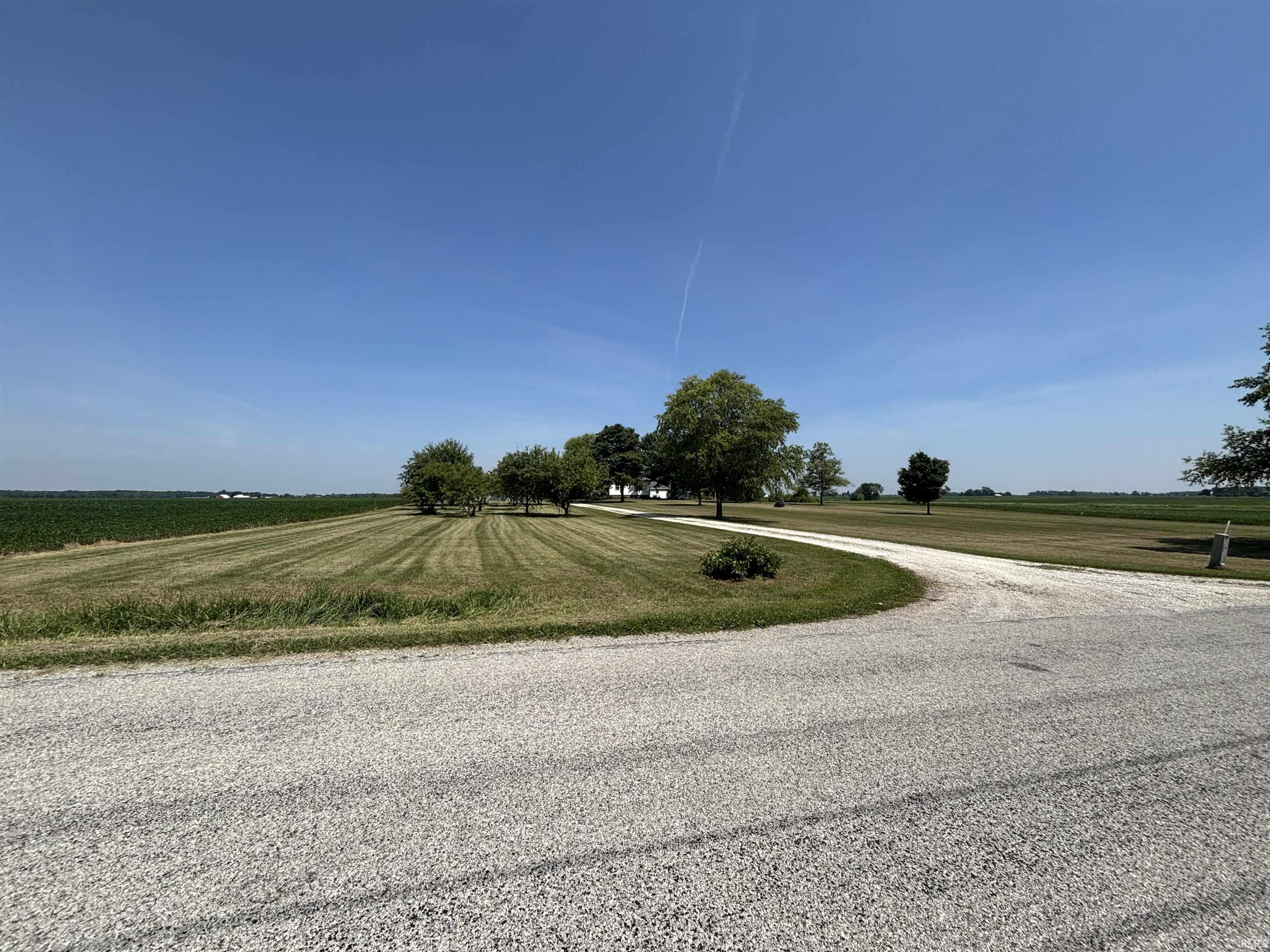Gravel driveway approaching a property set amidst expansive green fields