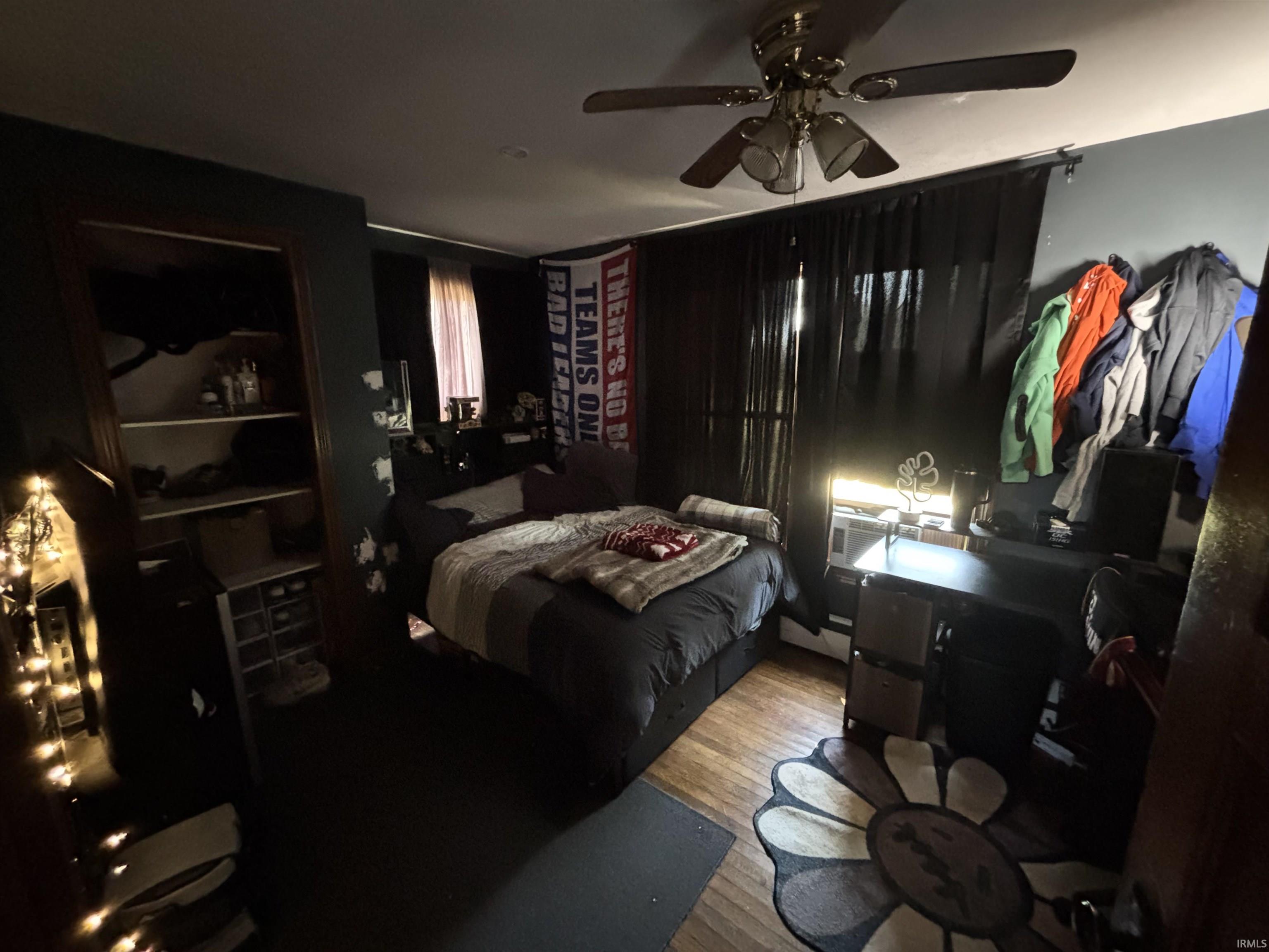 Room featuring wood-finish flooring, a ceiling fan with light fixture, and dark wall finishes