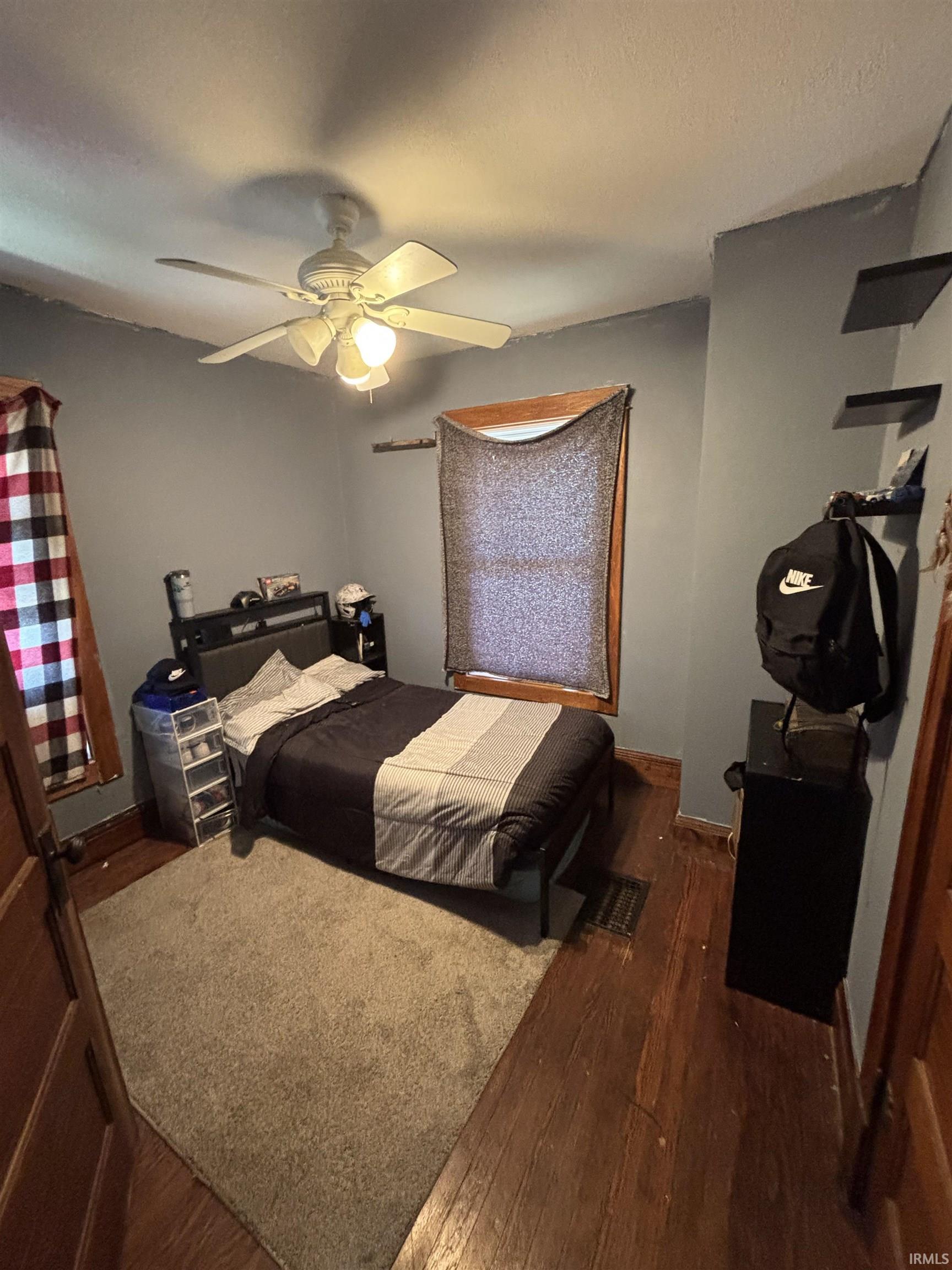 Room featuring wood-finish flooring, a ceiling fan with integrated lighting, and two windows with wood trim