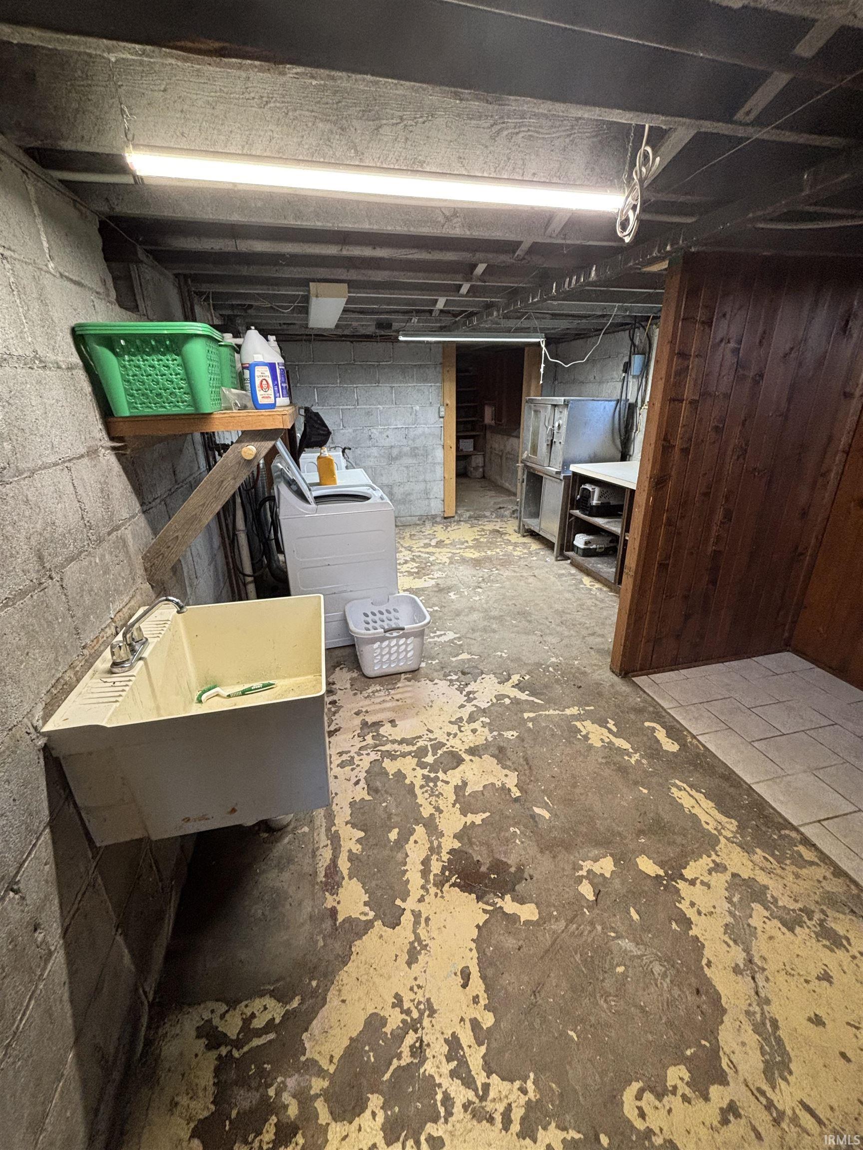 Utility basement featuring exposed ceiling joists, concrete block walls, a utility sink, and partial wood-paneling