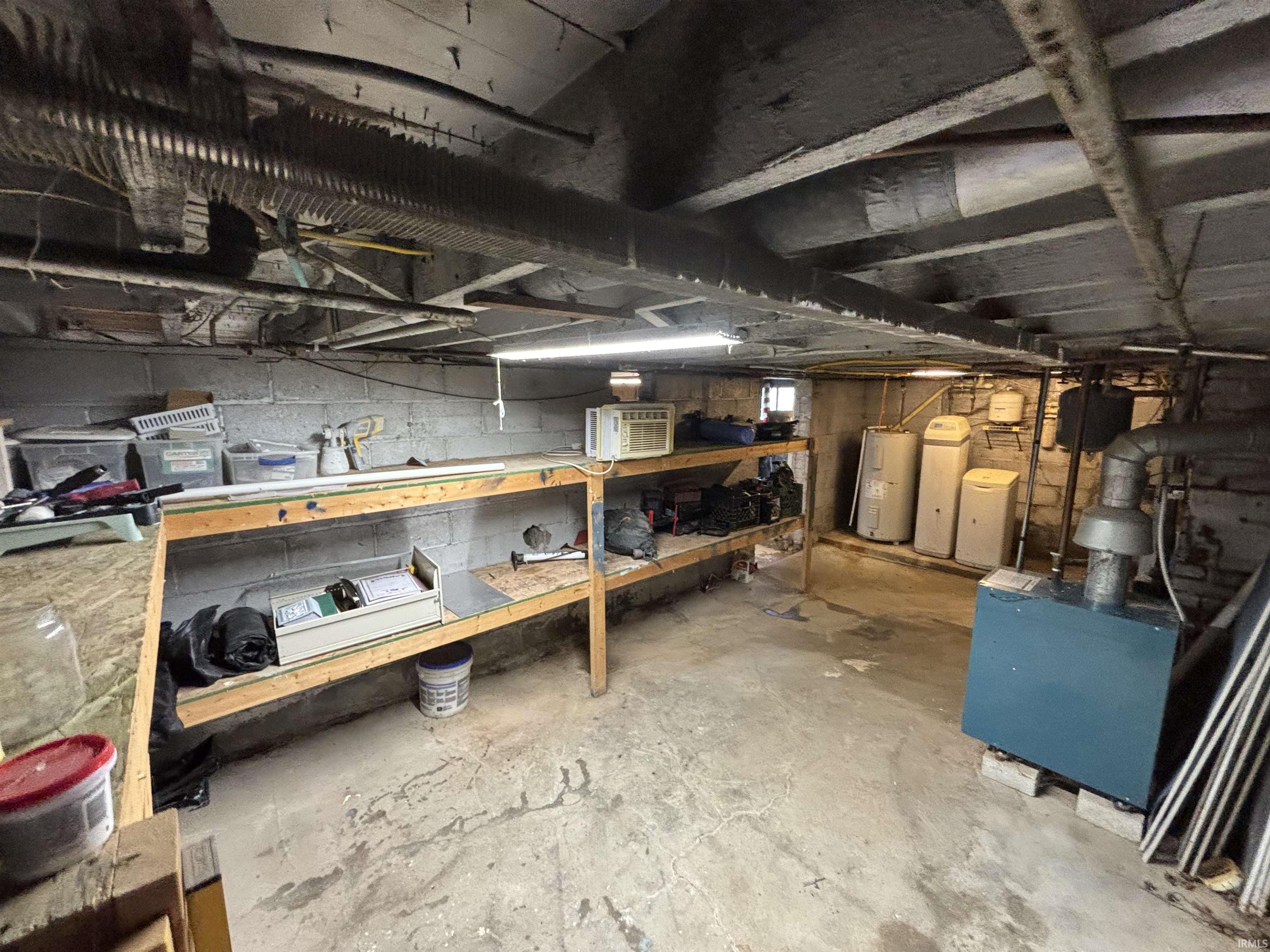 Concrete floor basement featuring exposed ceiling joists, built-in wooden shelving, a utility area with water heaters, and a floor-standing boiler