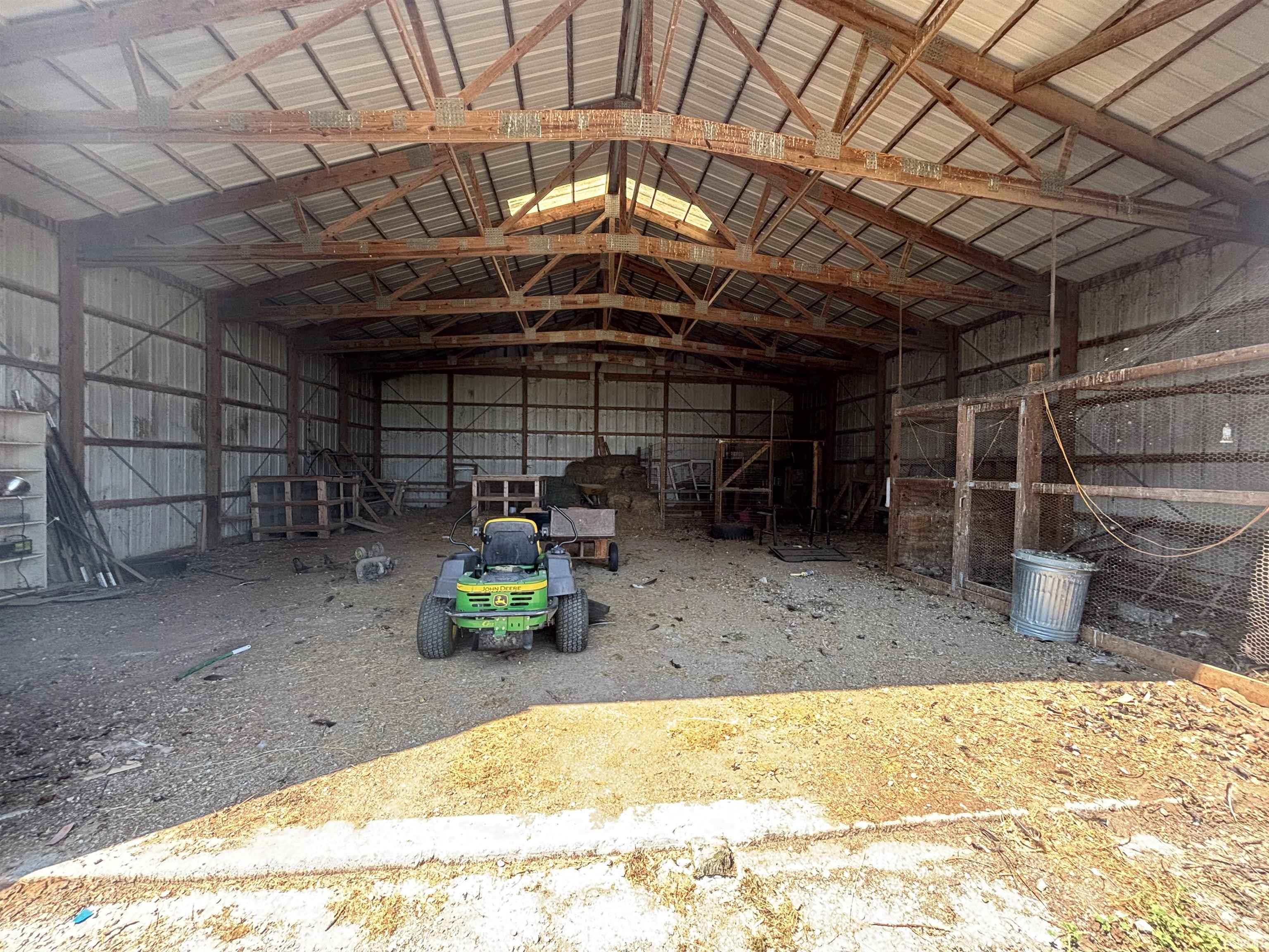 Expansive barn interior featuring a metal roof, exposed wooden trusses, corrugated metal walls, and a dirt floor
