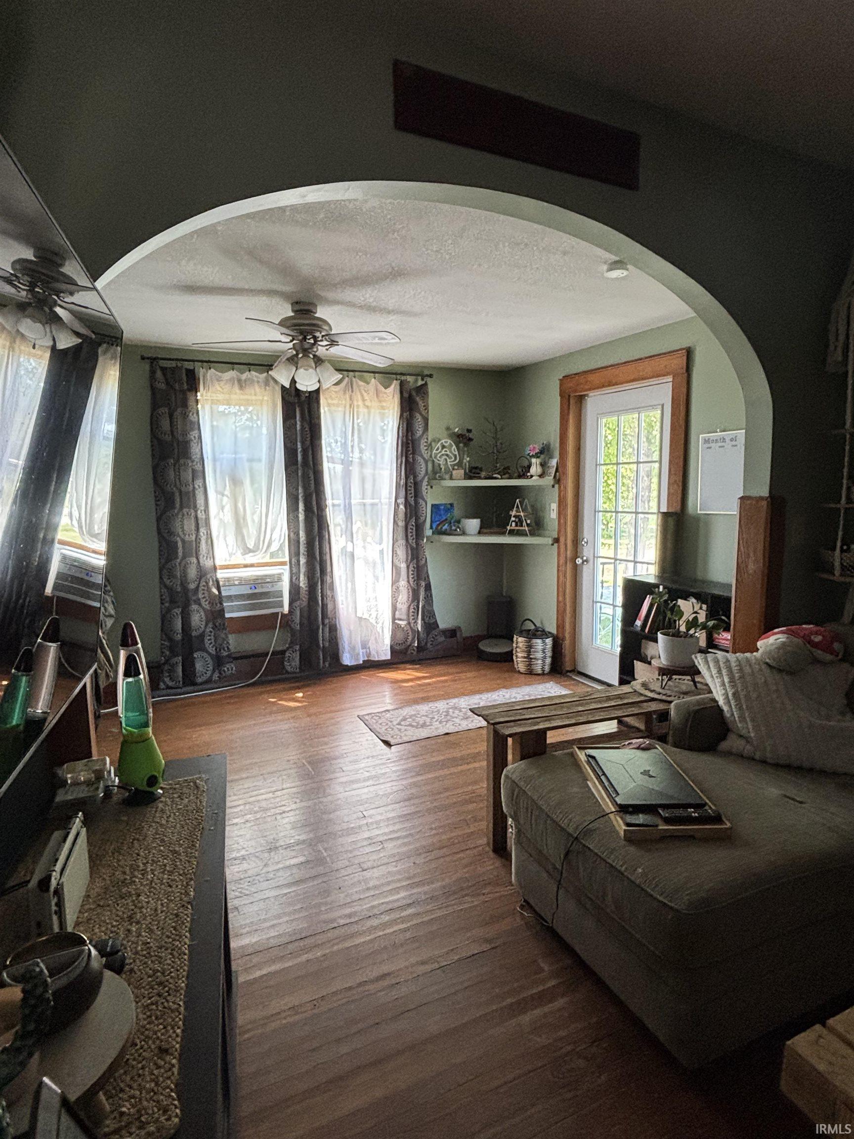 Living area featuring wood-finish flooring, a ceiling fan with integrated lighting, and an arched doorway