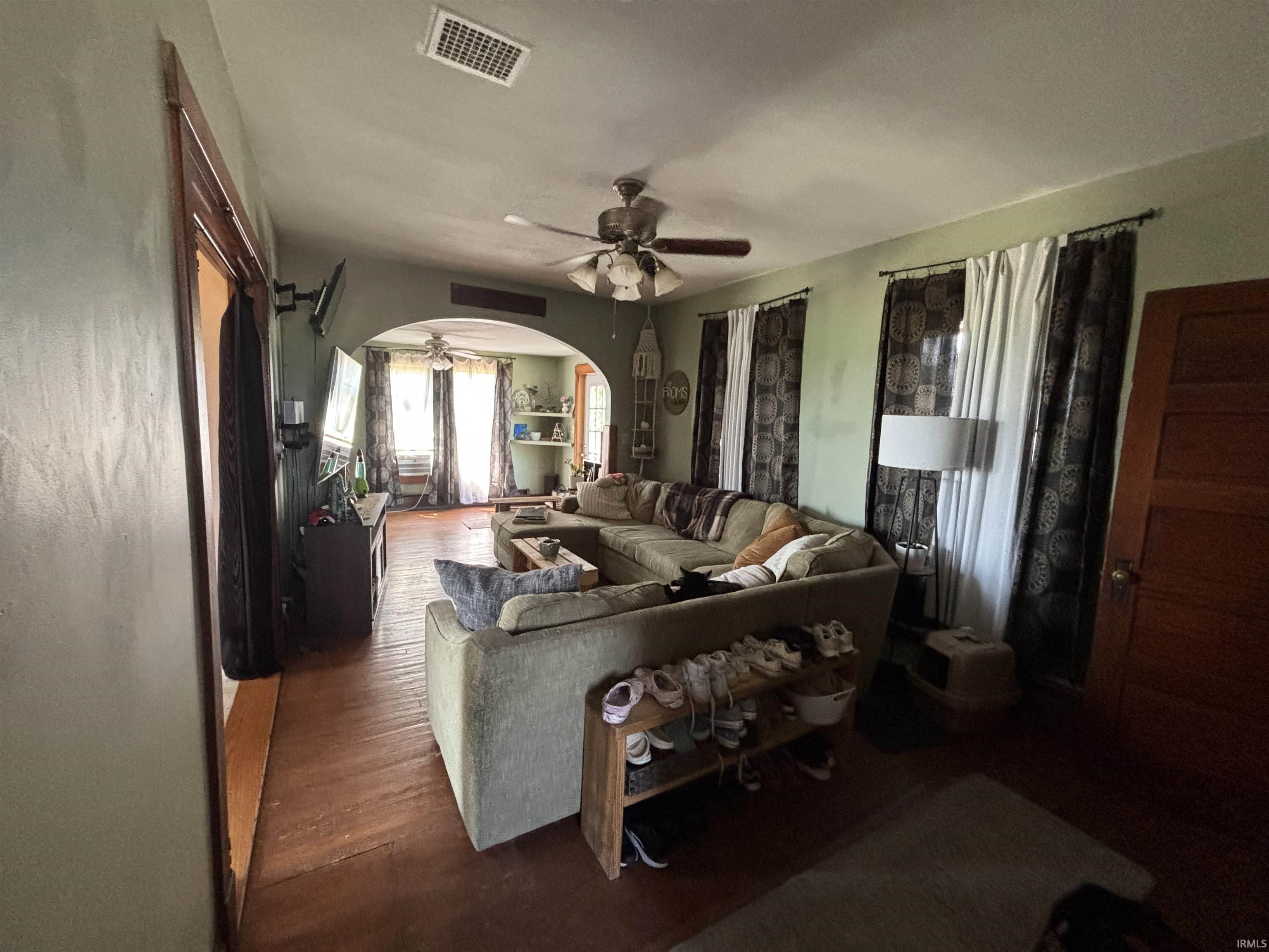 Spacious living area featuring wood-finish flooring, an arched doorway, and multiple windows