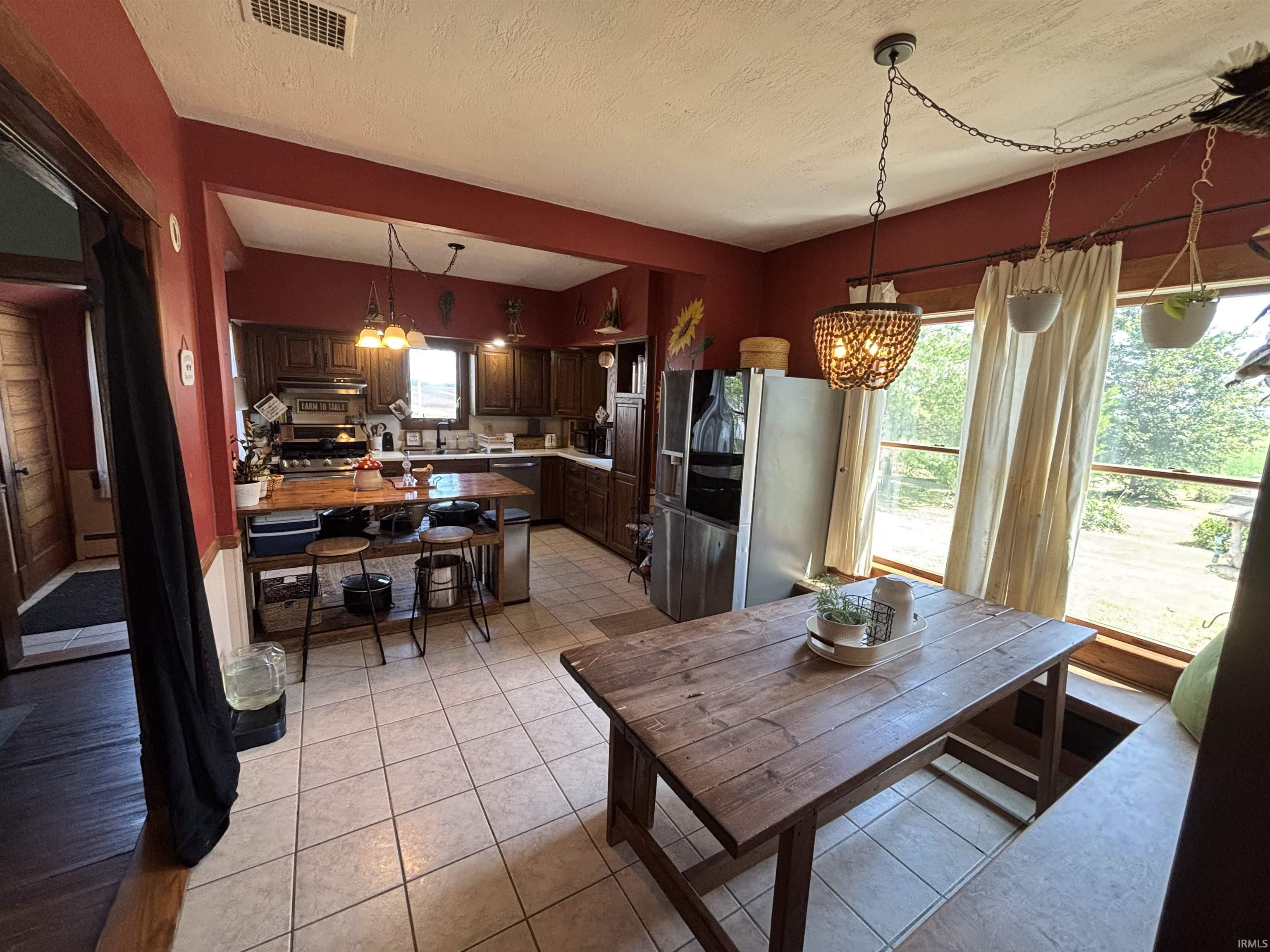 Spacious kitchen and dining area featuring ceramic tile flooring, dark wood cabinetry, a stainless steel refrigerator, a built-in window bench, and a wood-finish dining table