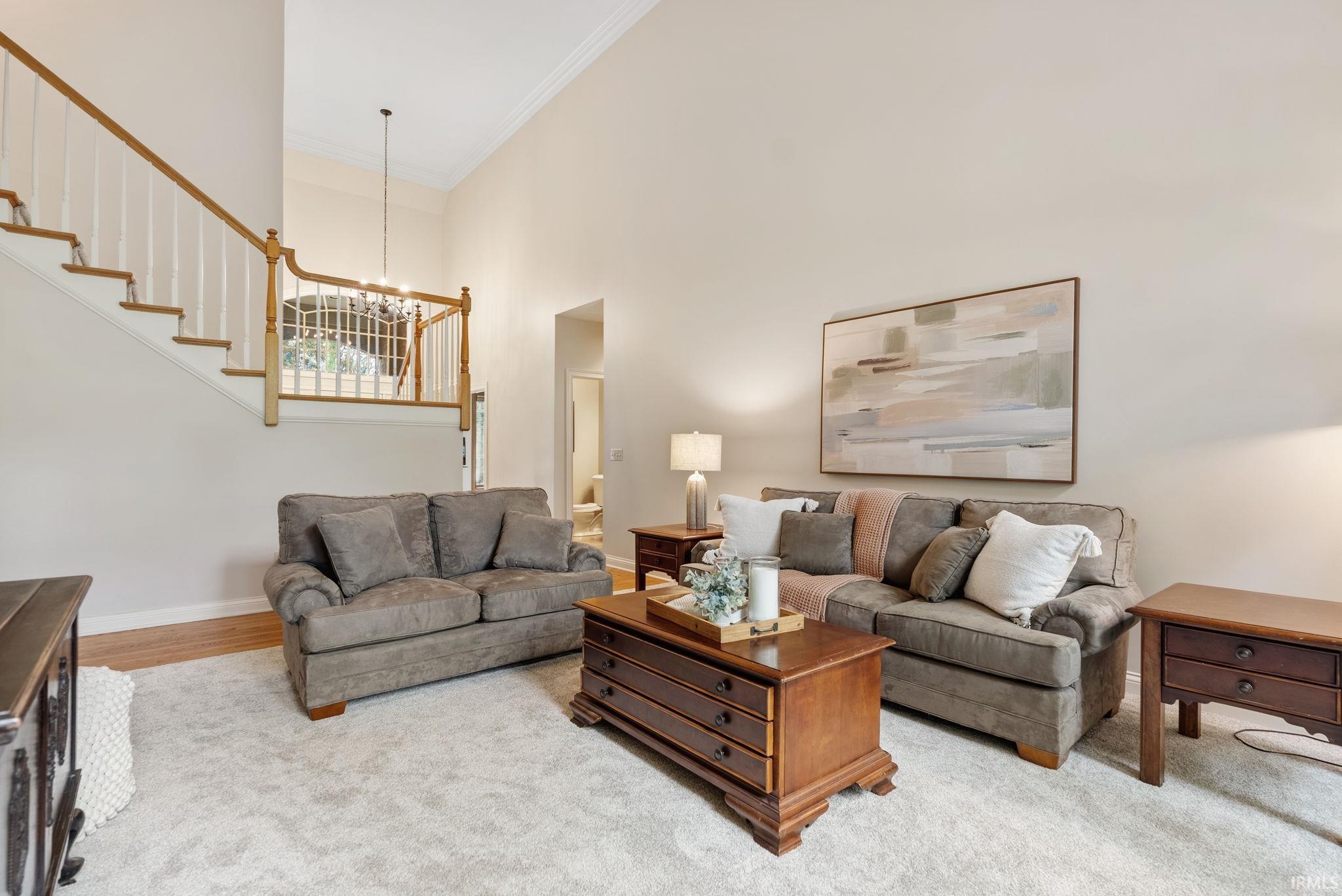 Two-story living area featuring vaulted ceilings, light-colored wall paint, and a carpeted floor
