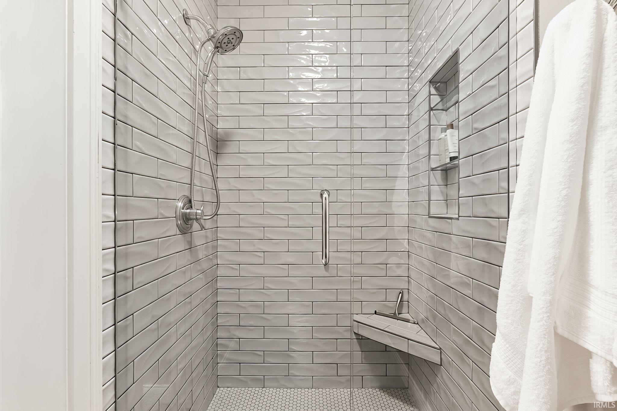 Shower stall featuring textured subway tile walls, a built-in corner bench, a recessed niche with glass shelving, and a hex tile floor
