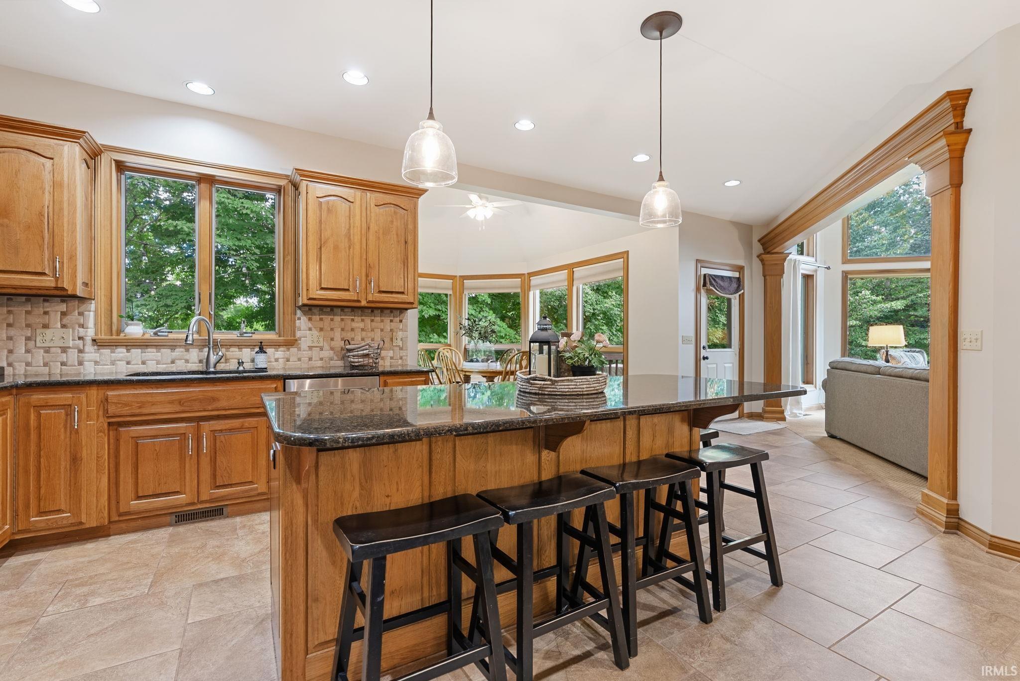 Kitchen featuring wood cabinetry, a large central island with seating, granite countertops, and a tile backsplash