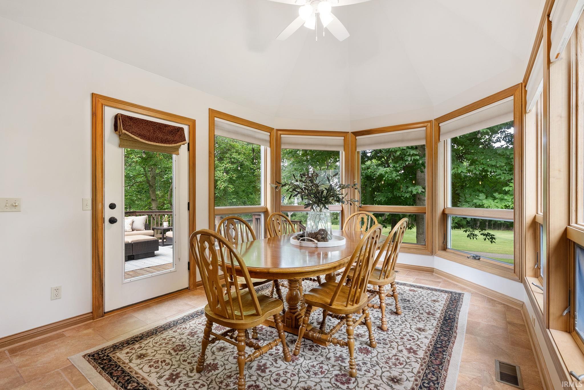 Sunroom featuring a vaulted ceiling with a ceiling fan, multiple large windows, natural wood trim, and tile flooring