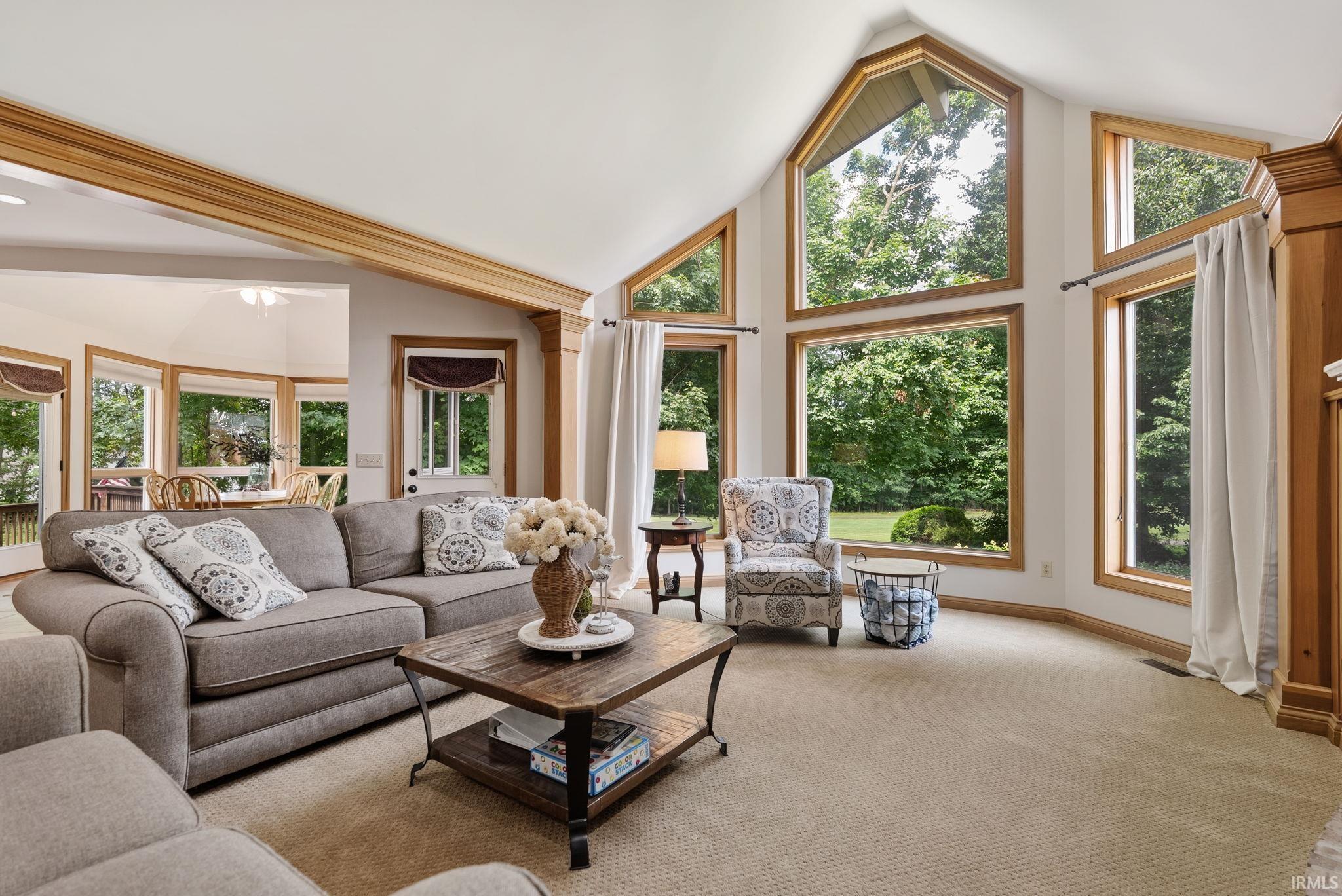 Vaulted ceilings with natural wood trim, expansive window array, and neutral carpet flooring