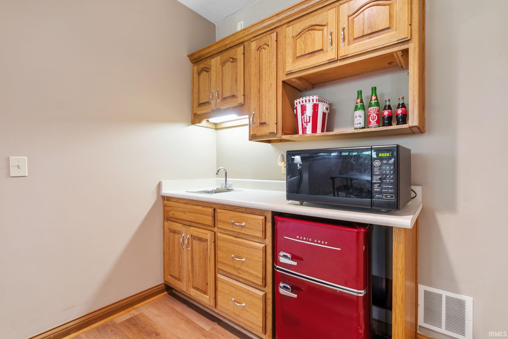 Compact kitchenette featuring wood-finish cabinetry, a built-in sink, and a light-toned countertop