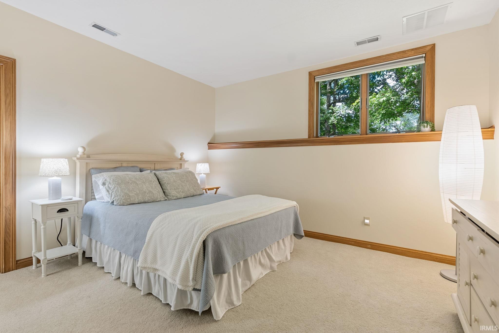 Carpeted bedroom featuring a wood-trimmed window, neutral wall paint, wood baseboards, and a built-in wall light