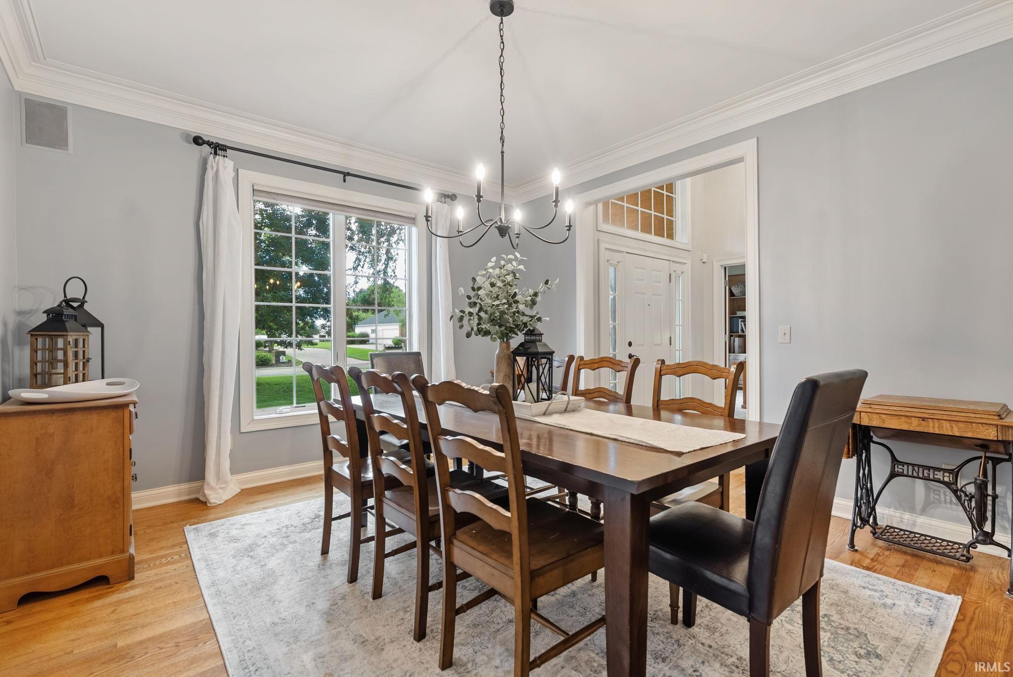 Spacious dining area featuring hardwood flooring, crown molding, a window with grid patterns, a black chandelier, and light gray wall tones