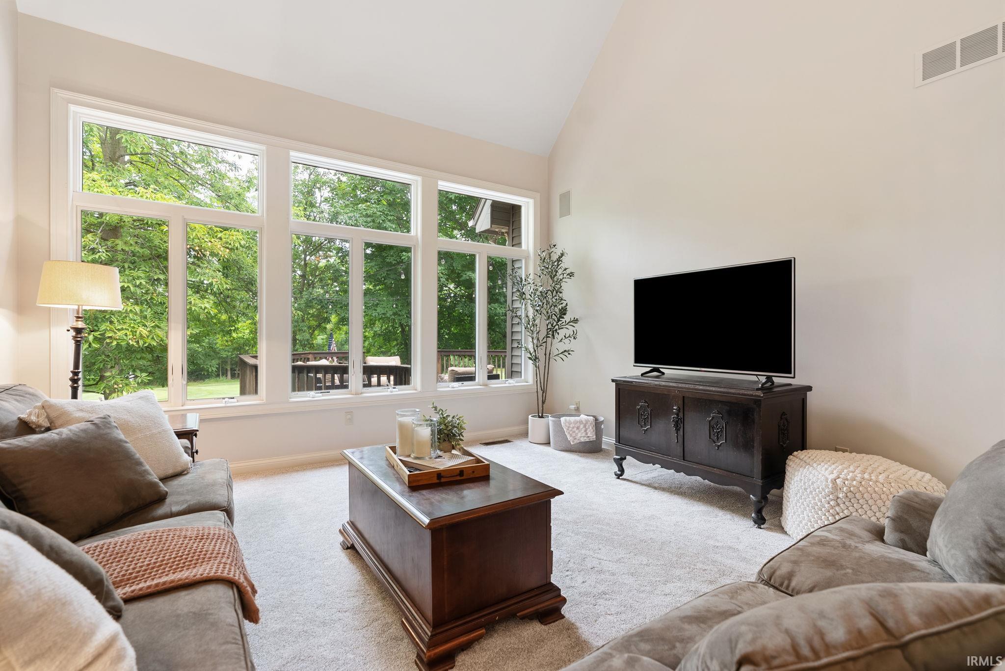 Living area with vaulted ceiling, light-toned carpeting, and a wall of windows featuring white trim