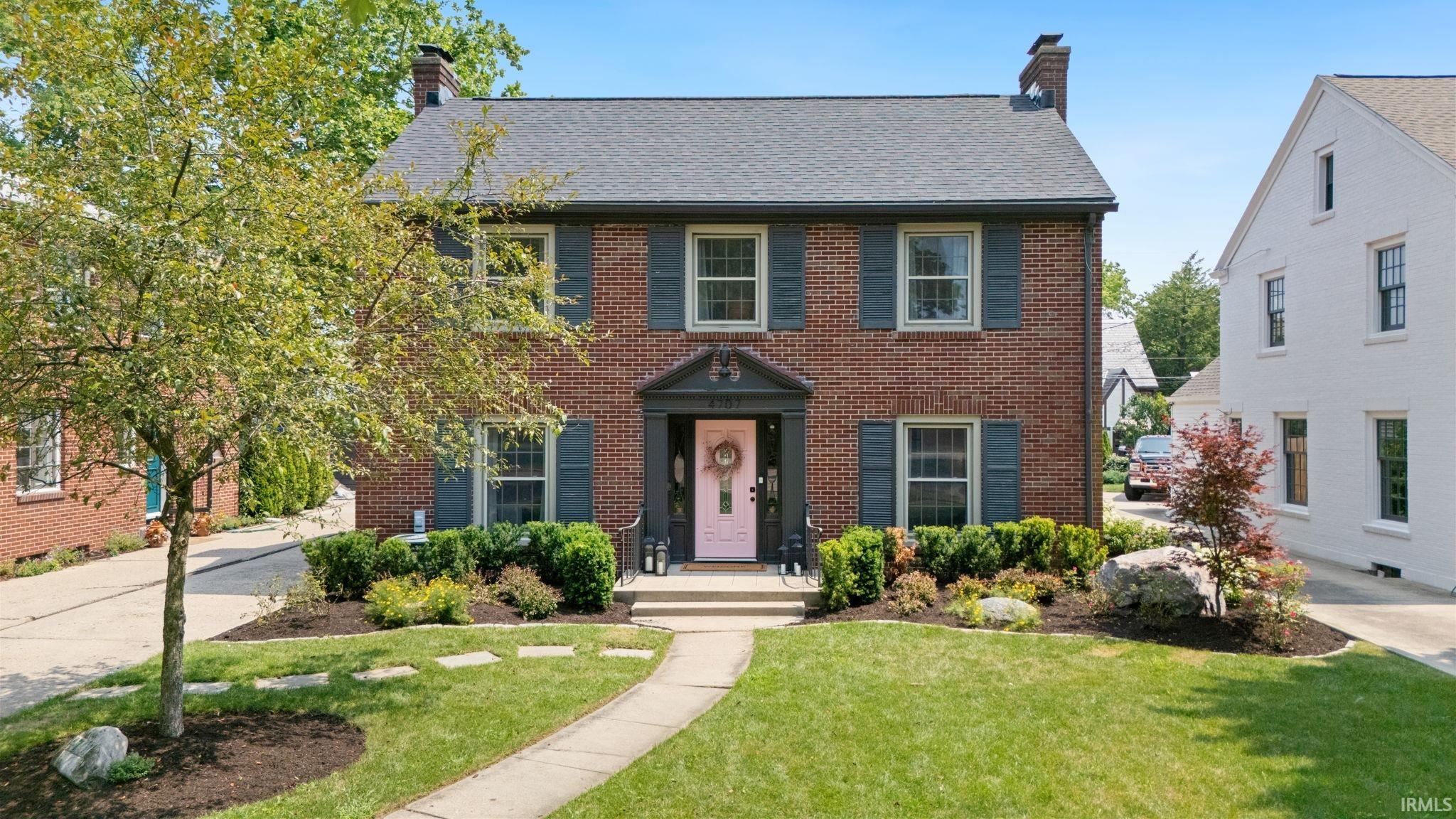 Brick facade featuring a black shingled roof, dark grey shutters, and a pink front door