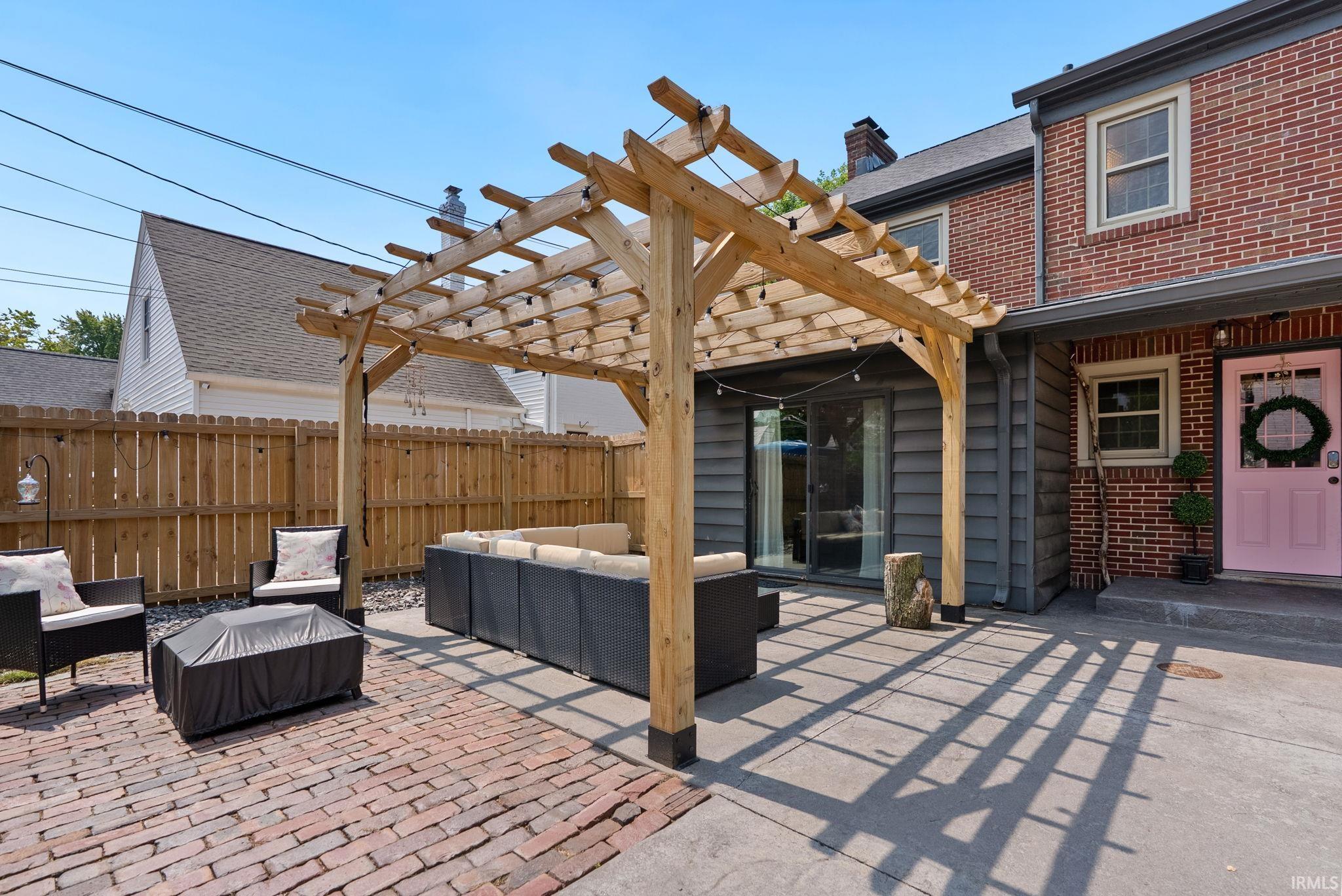 Outdoor patio featuring a natural wood pergola, brick paver flooring, and a sliding glass door entry