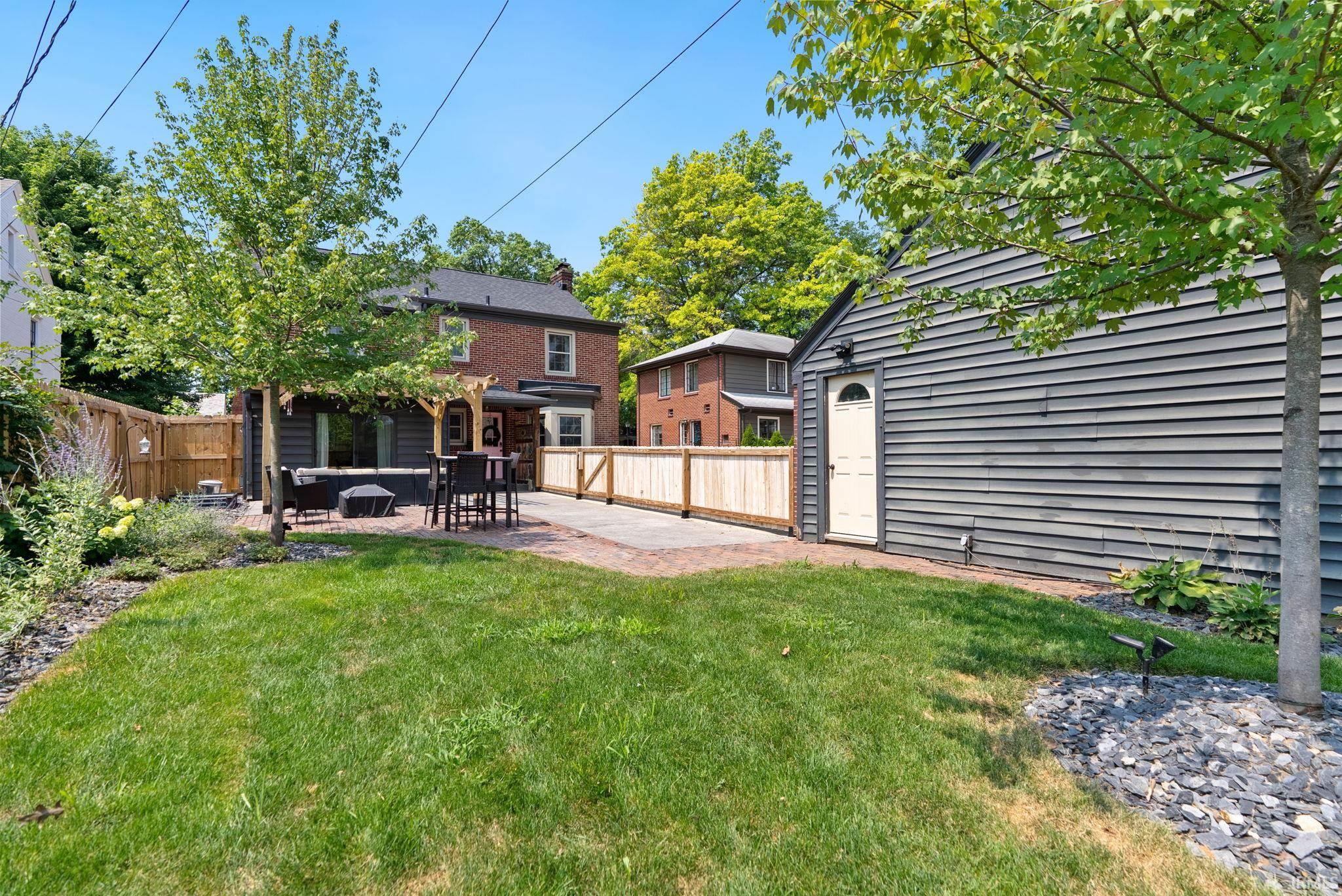 Expansive backyard featuring a manicured lawn, a brick patio with pergola, and a privacy fence