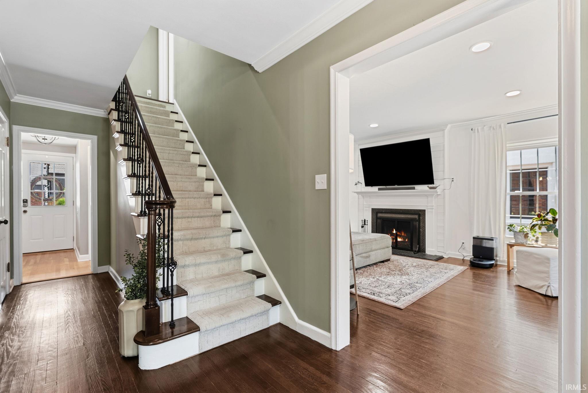 Hardwood flooring throughout the entry, staircase with carpeted treads and wrought iron balusters, white trim, and a white interior door with decorative glass panels