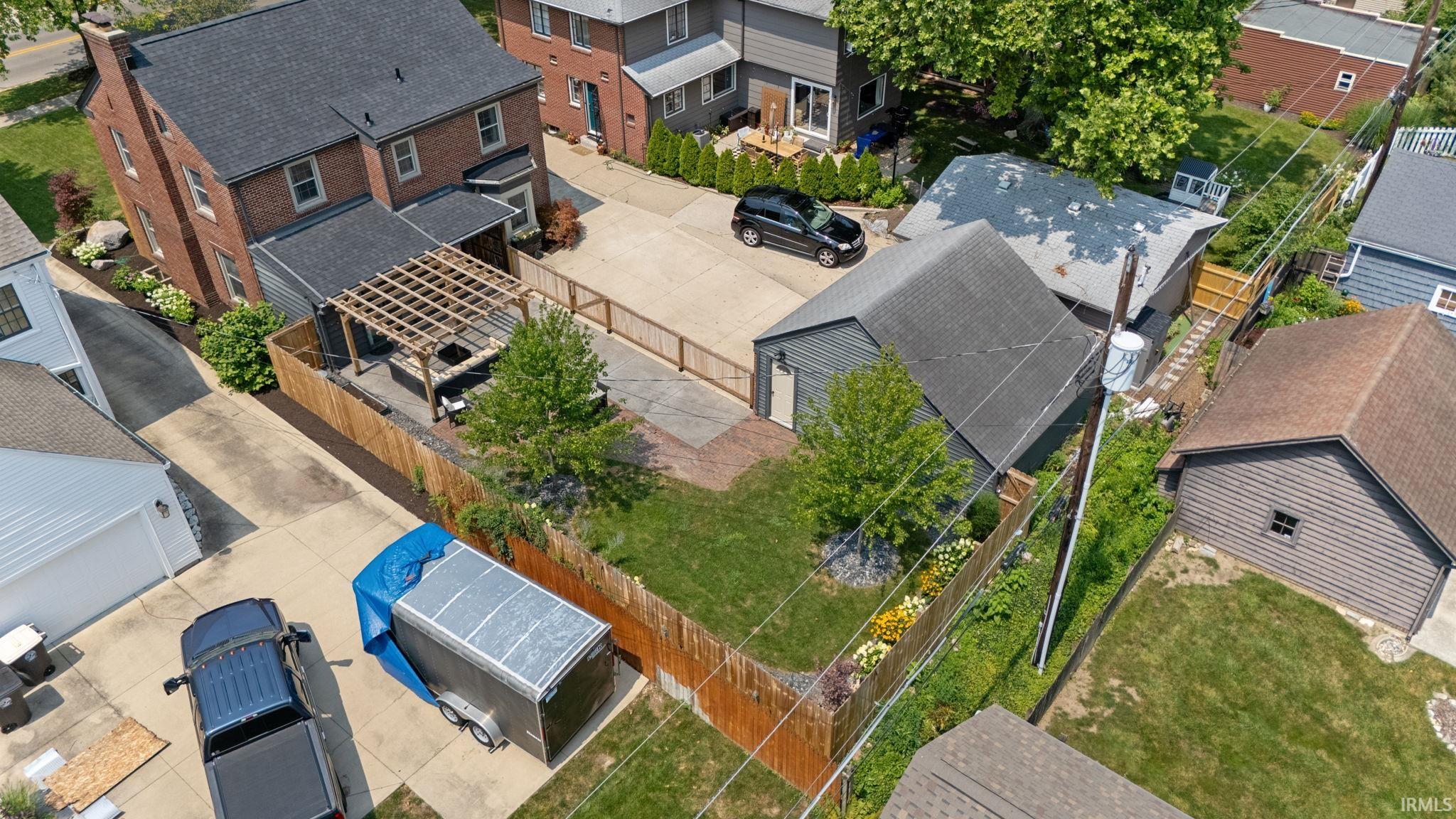 Brick exterior residence featuring a rear patio with a wooden pergola, a detached garage with a gray roof, a fenced backyard with green lawn, and mature perimeter landscaping