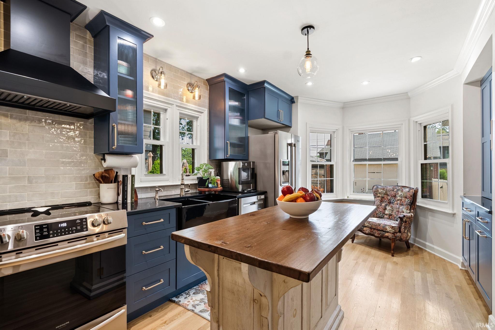 Kitchen featuring blue cabinetry, a wood-finish island countertop, stainless steel appliances, and light wood-finish flooring