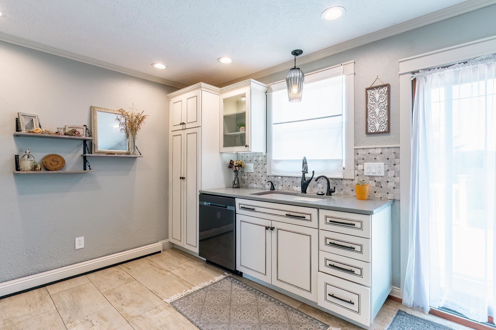 Kitchenette featuring white cabinetry with dark hardware, a gray countertop, mosaic tile backsplash, and a built-in sink with a matte black faucet