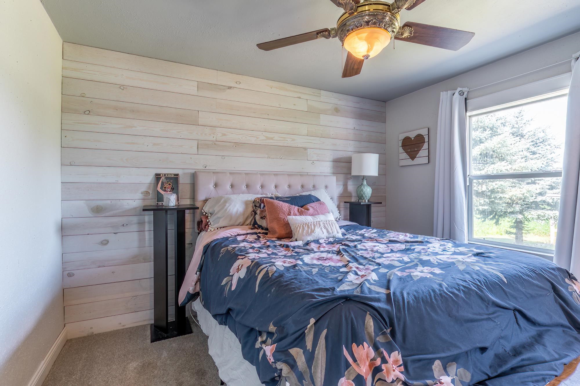 Bedroom featuring a decorative wood plank accent wall, neutral carpeting, and a window with white drapes