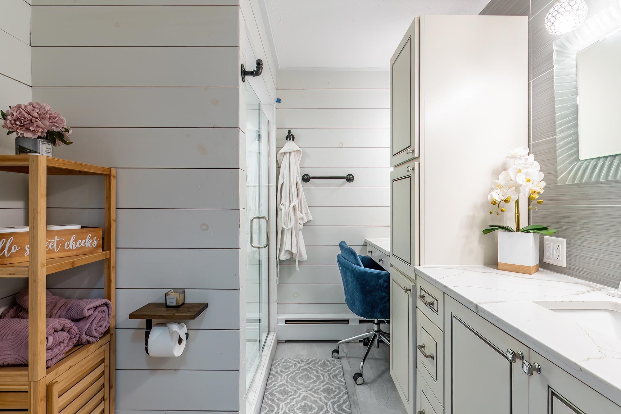 Bathroom featuring white shiplap walls, a glass-enclosed shower, a vanity with a white countertop and integrated sink, and built-in cabinetry
