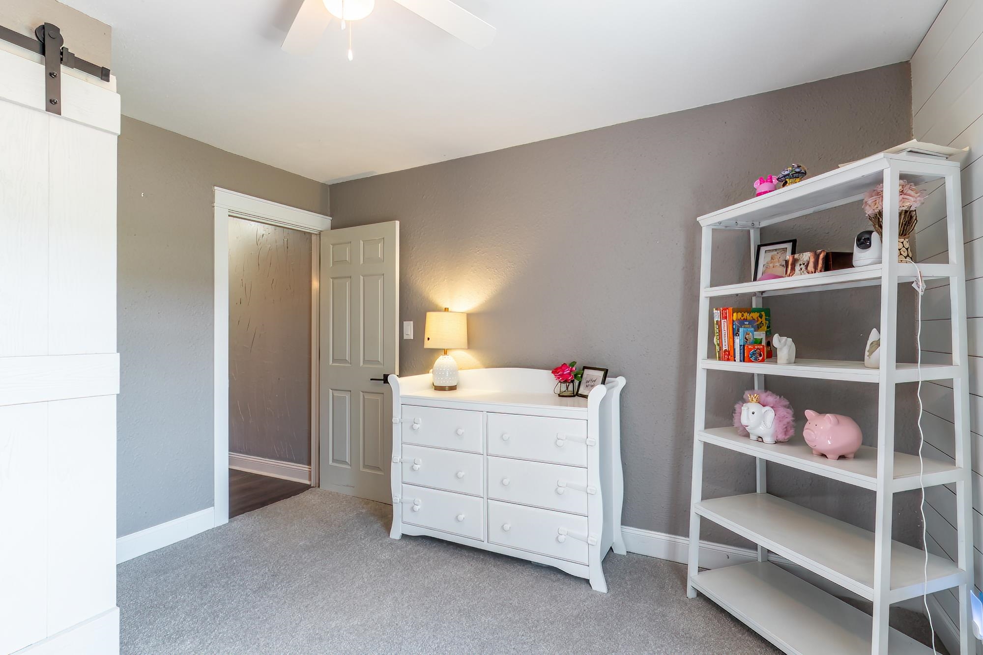 Carpeted room featuring a ceiling fan, a barn door, and a traditional paneled door leading to another area