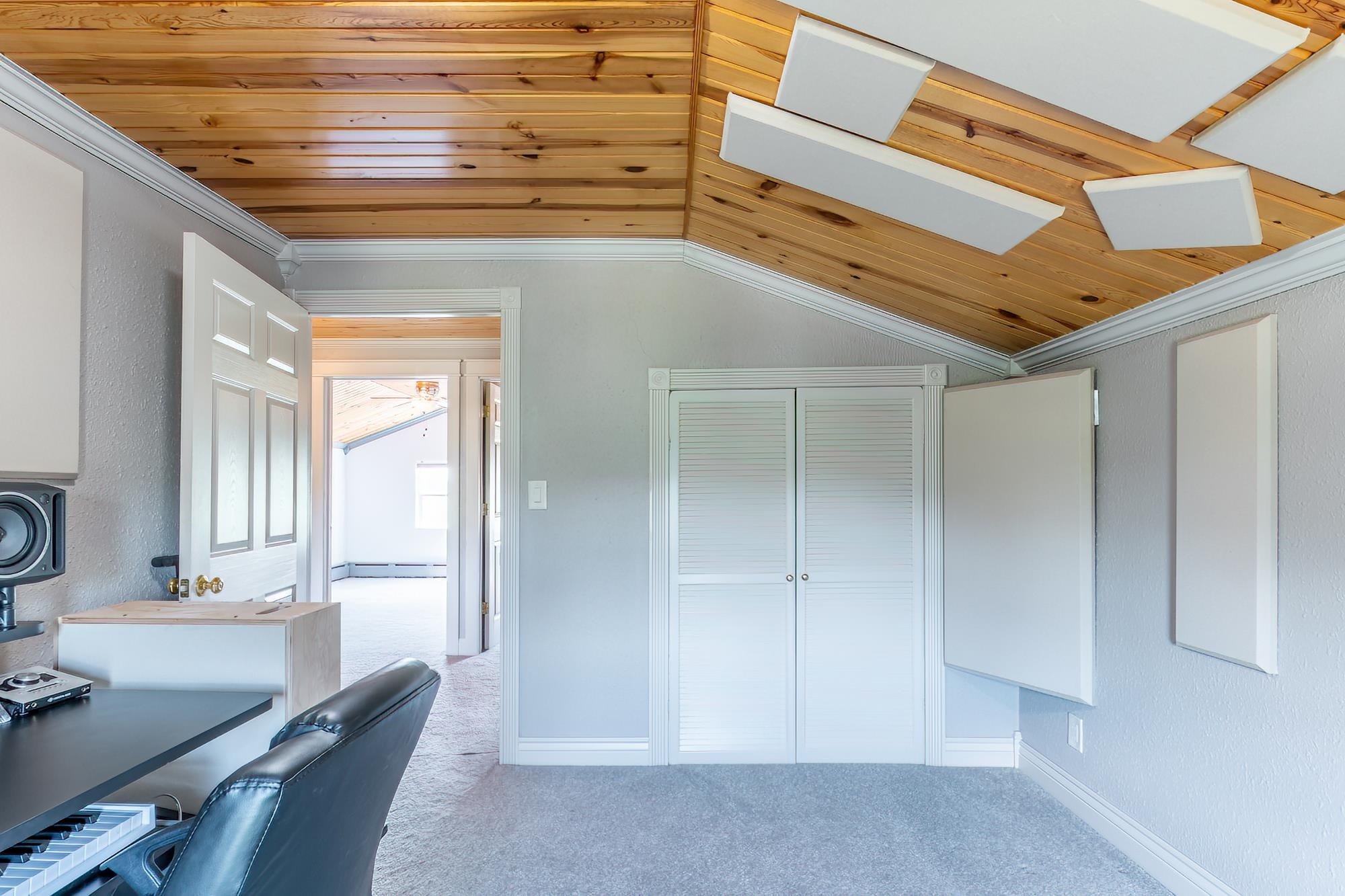 Room featuring an angled wood-finish ceiling with acoustic panels, light gray textured walls, and light gray carpeting