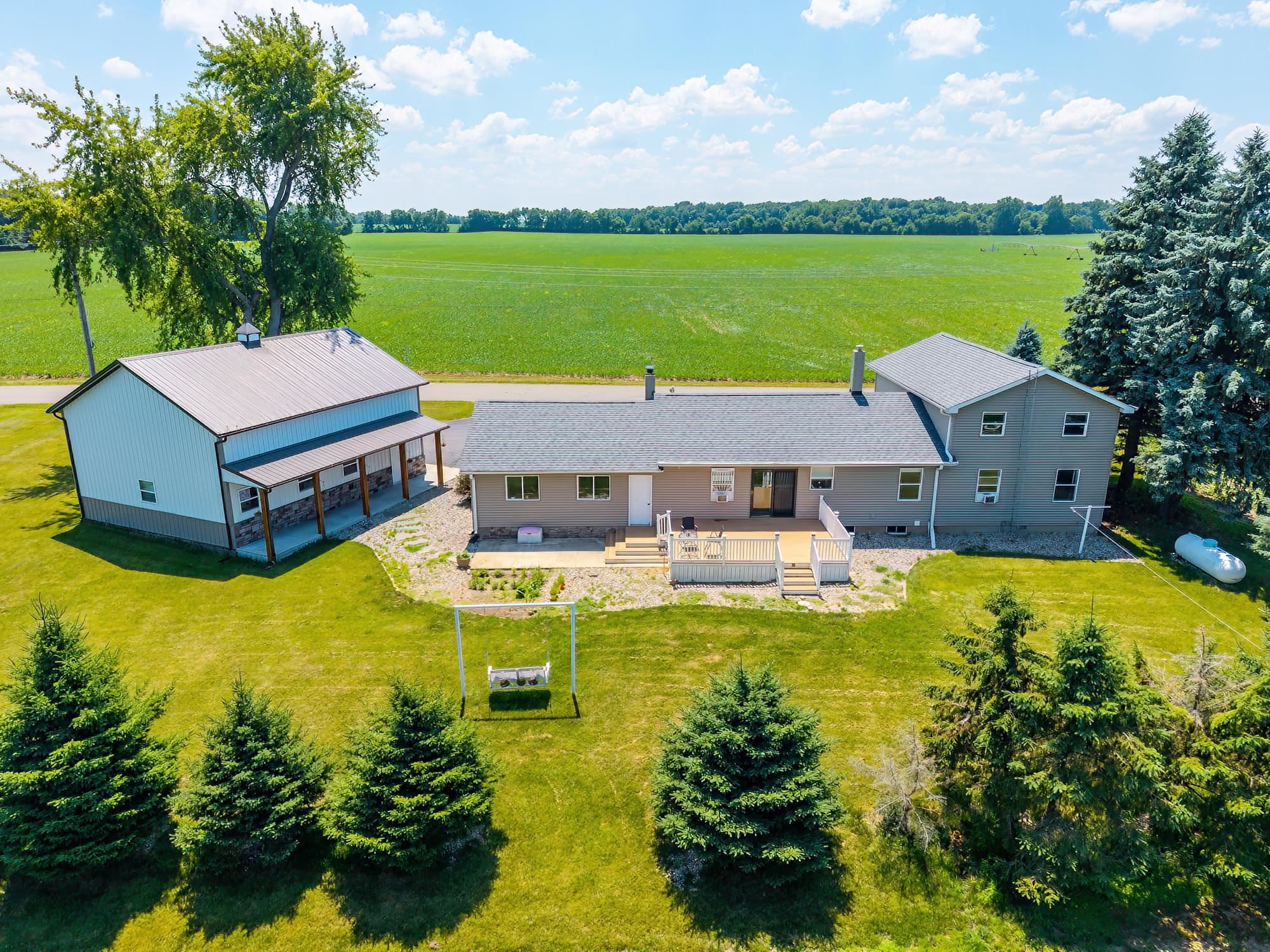 Expansive property featuring a multi-level residence with a wood deck, an additional outbuilding with a stone-accented porch, mature evergreen trees, and a spacious green lawn
