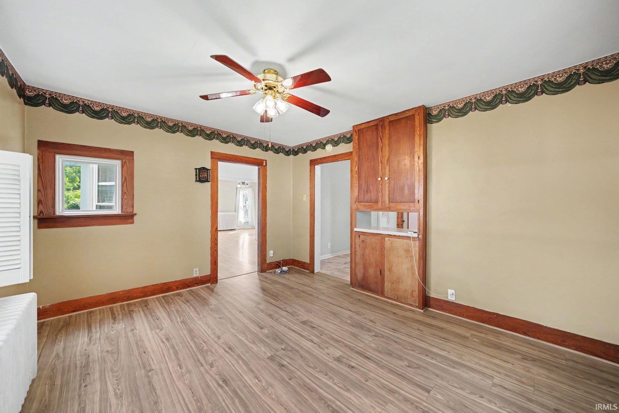 Room featuring wood-finish flooring, a built-in wood cabinet with upper and lower storage, and a ceiling fan with integrated lighting