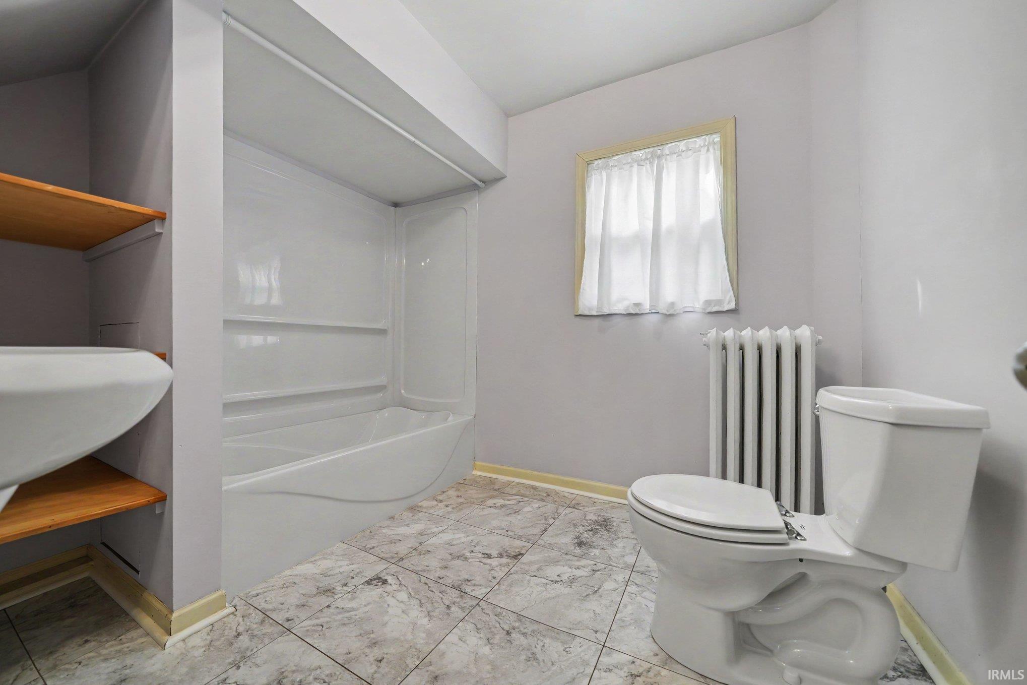 Bathroom featuring a tile floor, built-in bathtub with shower surround, toilet, and wood-finish shelving