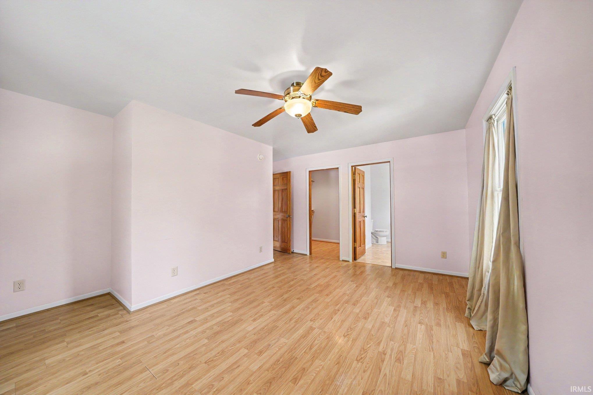 Spacious room featuring wood-finish flooring, a ceiling fan with integrated lighting, and multiple paneled doors