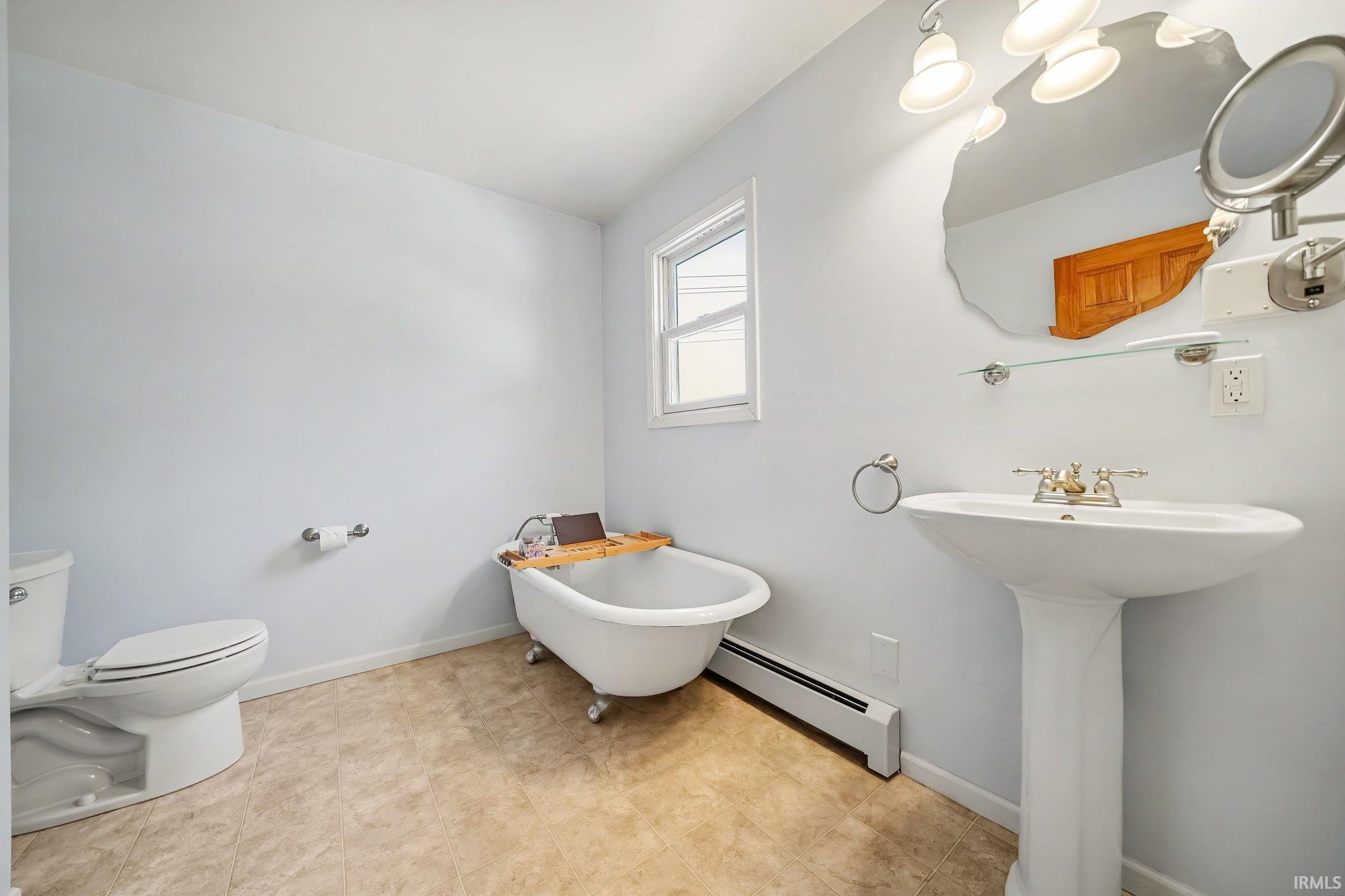 Bathroom featuring a freestanding clawfoot tub, pedestal sink with brass-finish fixtures, and a decorative wall mirror